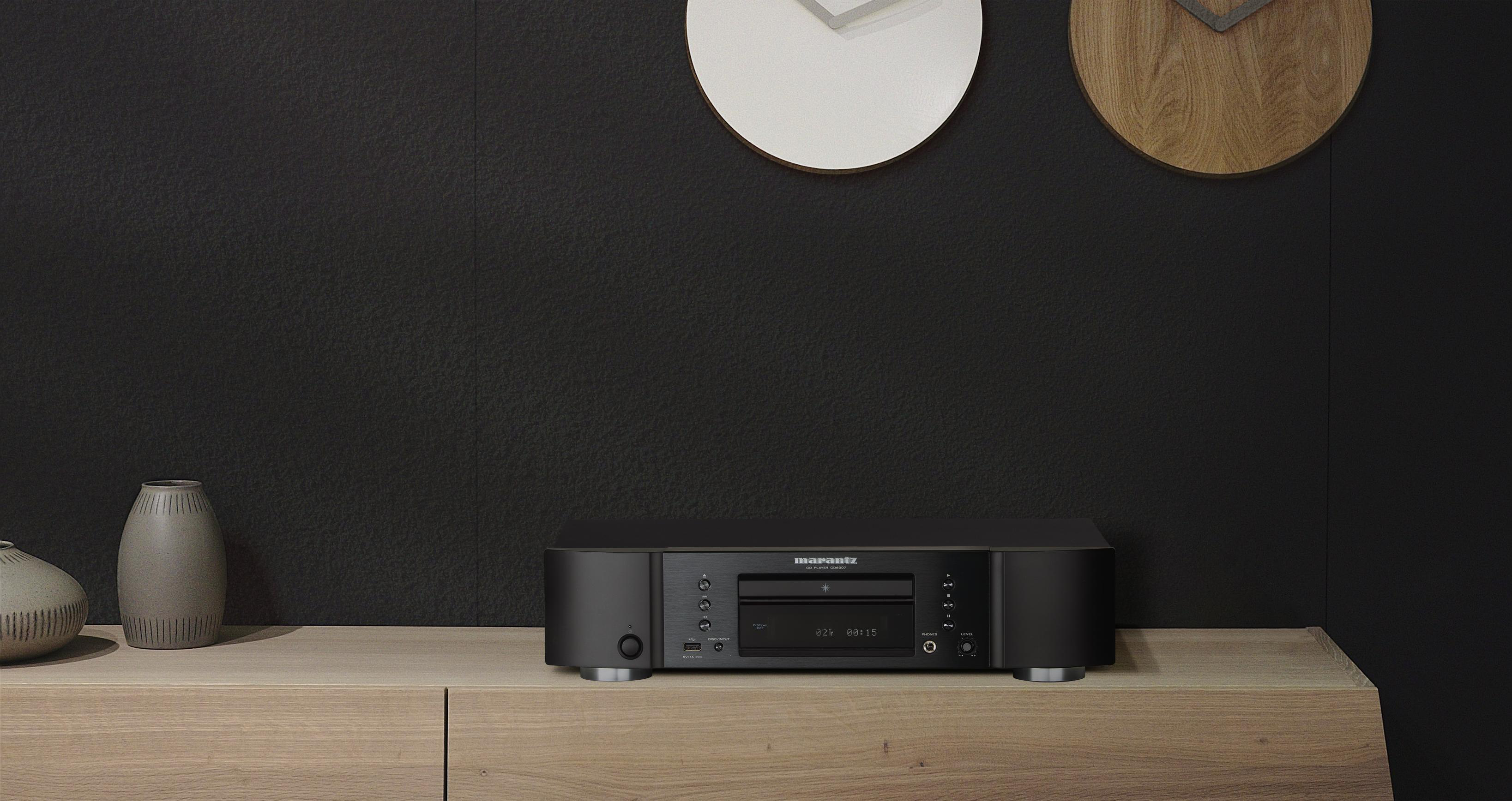 Ein schwarzer Audio-Receiver steht auf einem Holzschrank. Zwei Uhren und Vasen sind an der schwarzen Wand zu sehen.