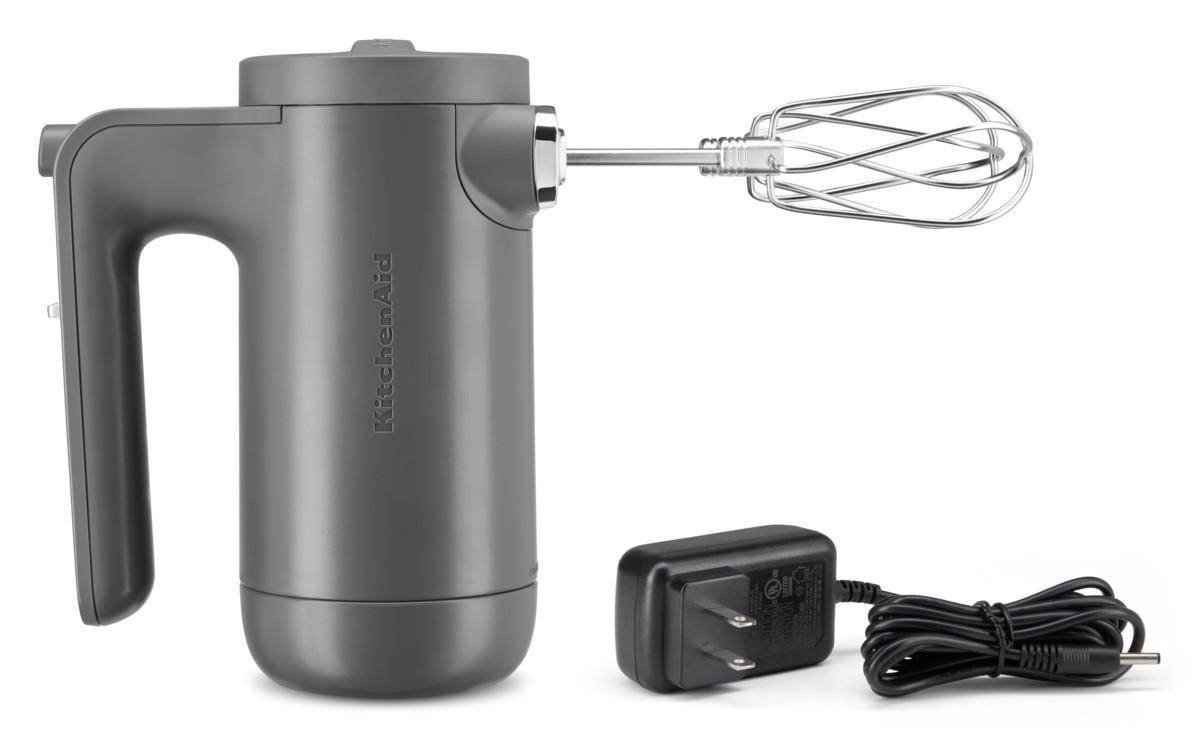 KitchenAid kabelloser Handmixer. Grau, mit Quirlaufsatz und Ladegerät. Weißer Hintergrund.