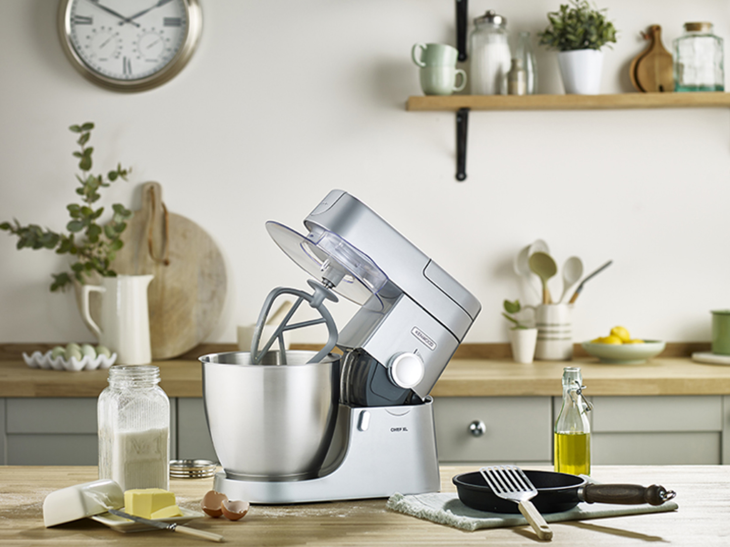 A silver kitchen stand mixer with ingredients on a wooden counter, and kitchen items.