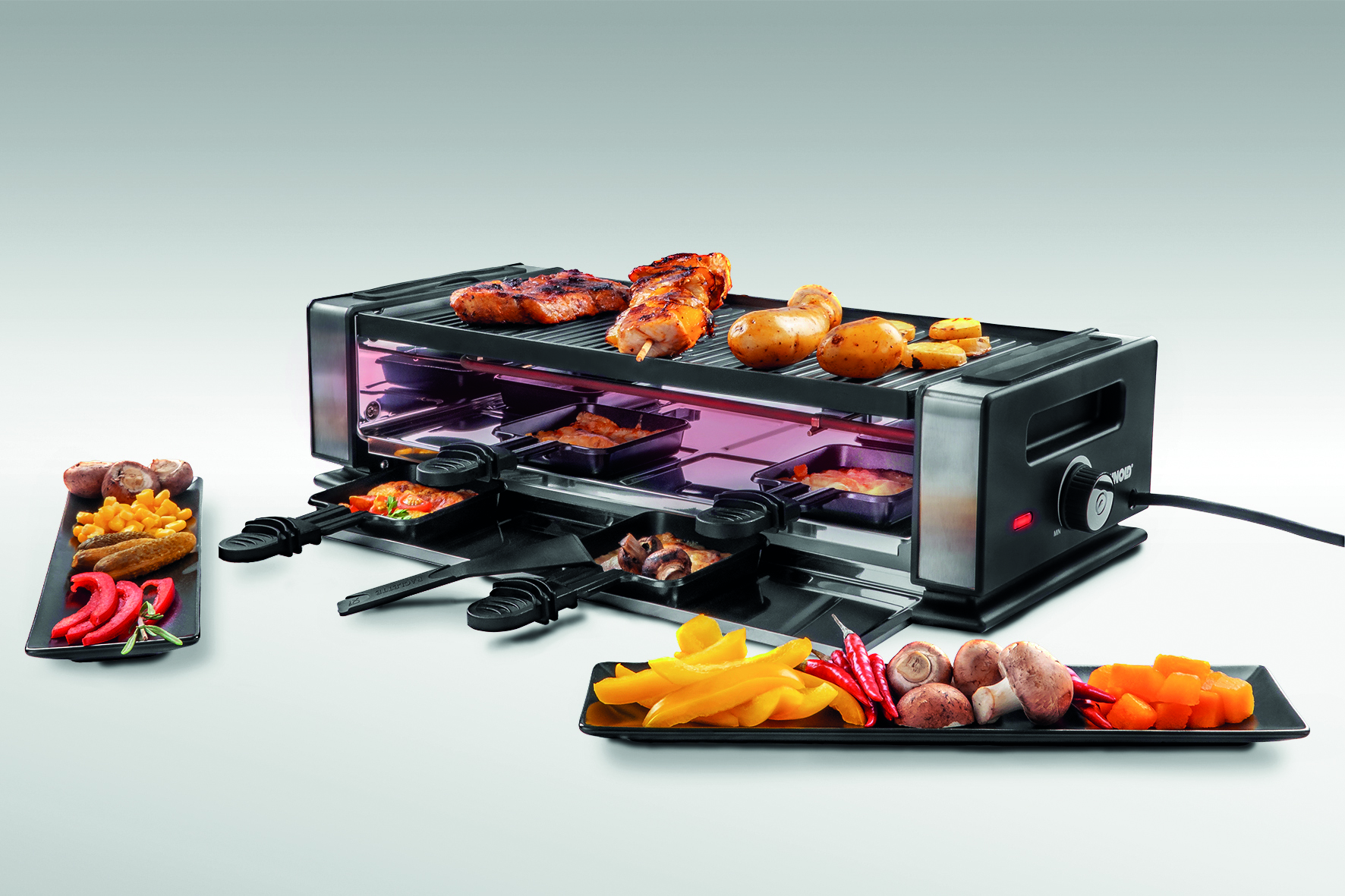 Raclette-Grill mit Essen: Fleisch, Kartoffeln, Gemüse. Gerichte an der Seite.