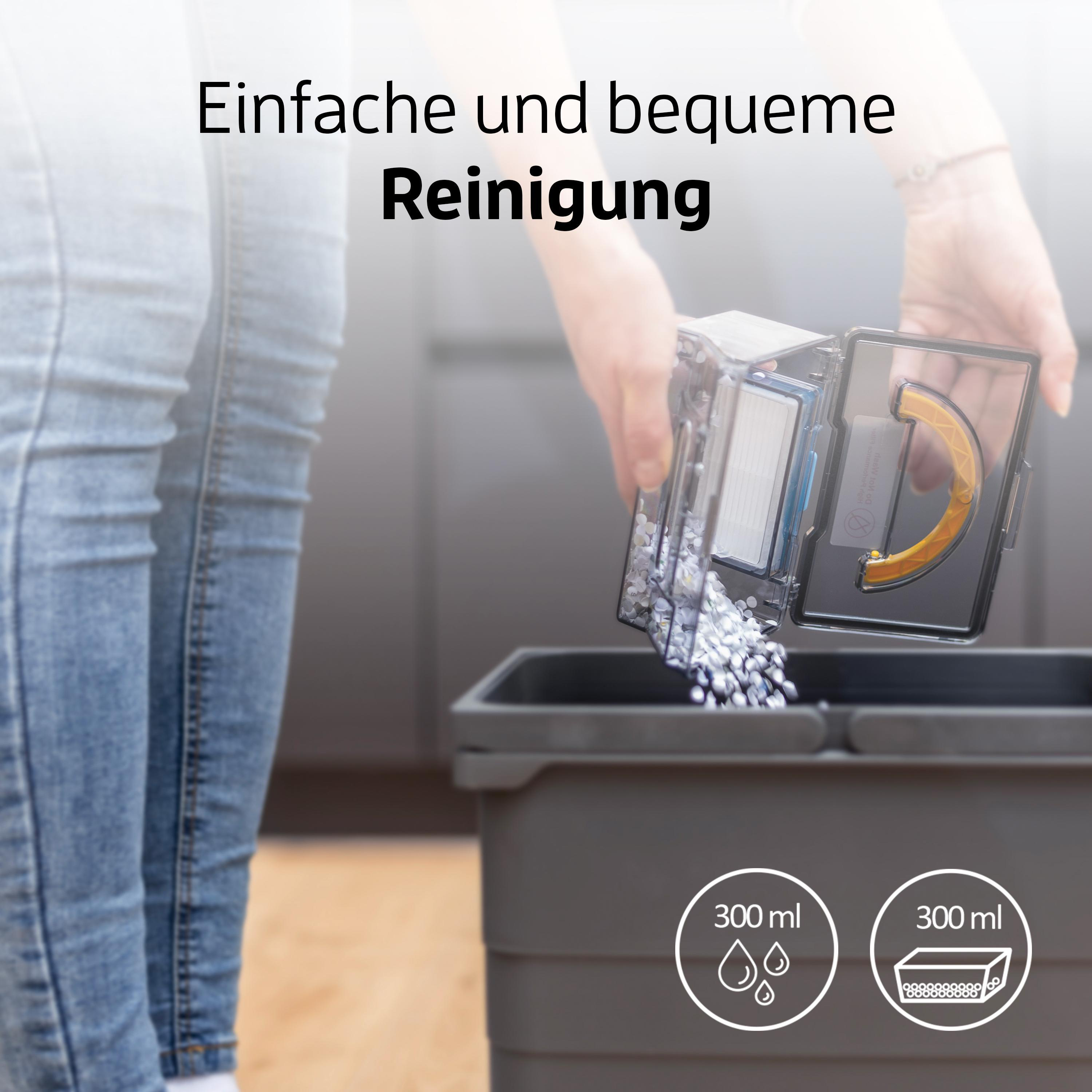 Eine Person entleert einen Staubsaugerbehälter in einen Mülleimer.