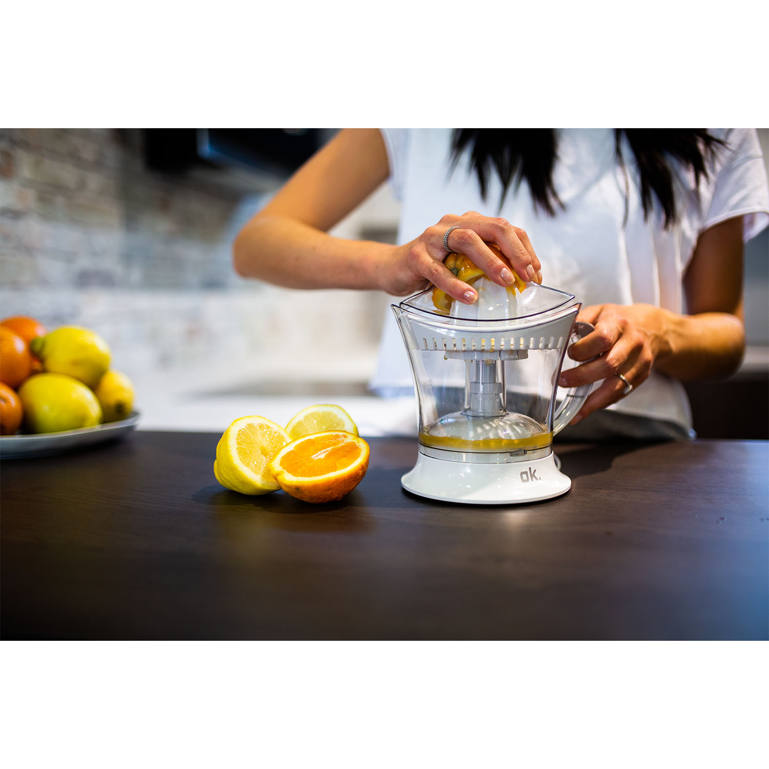 Una donna che spremi un limone in uno spremiagrumi, con arance e limoni su un bancone.
