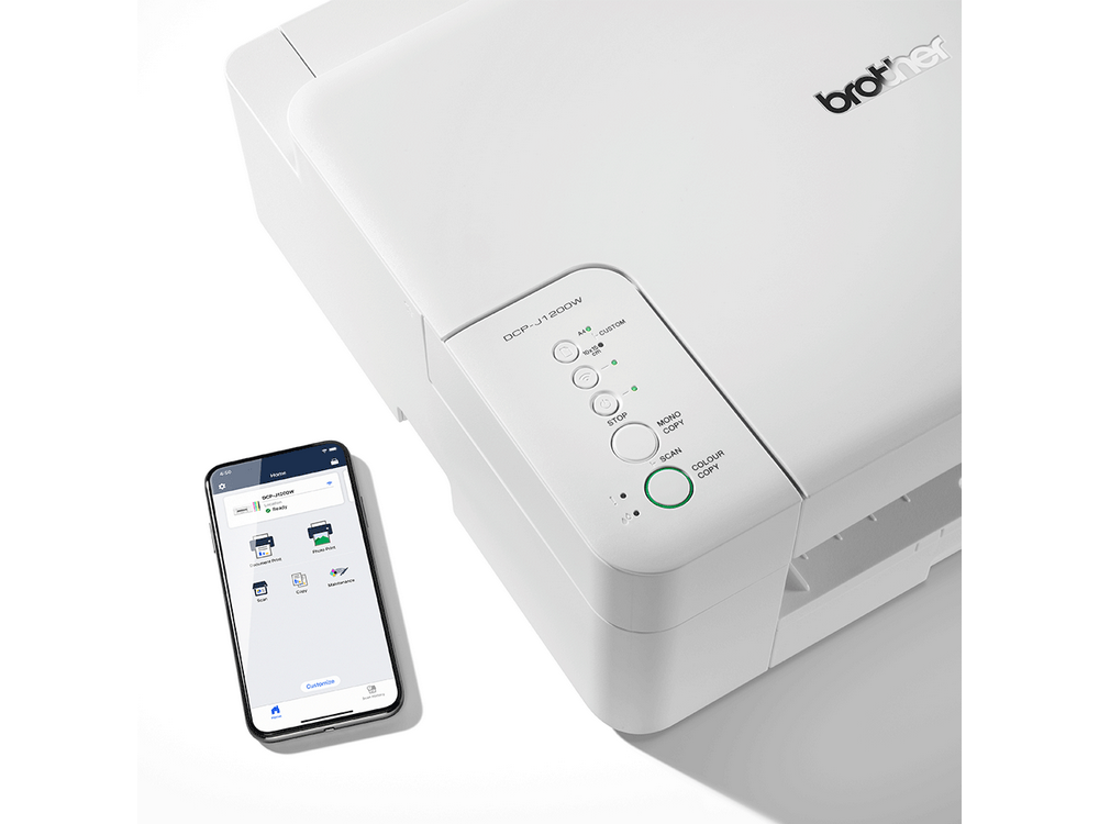 Impresora Brother blanca junto a teléfono con interfaz de app. Tiene panel de control y botones de copia.