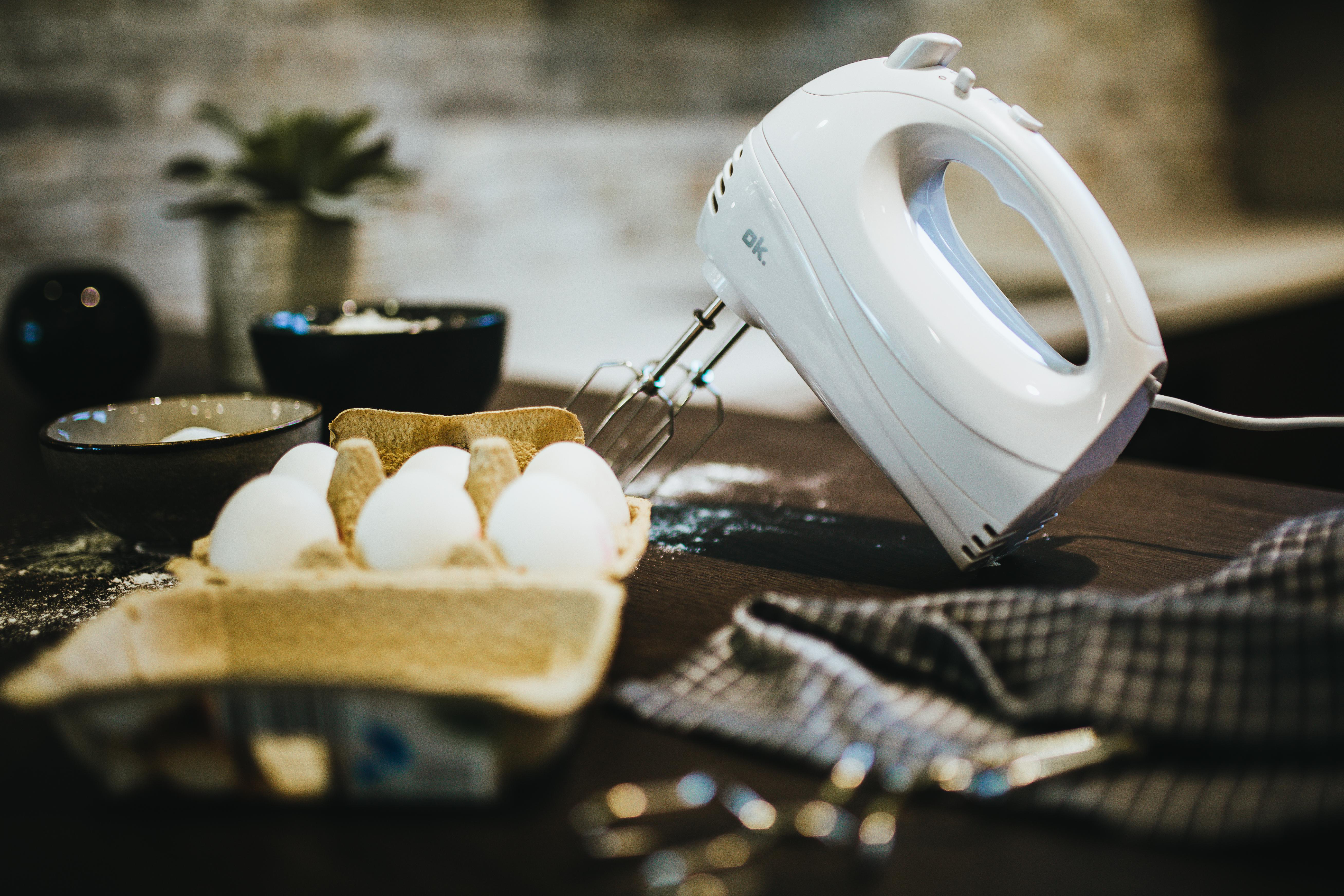 Eier im Karton, ein Mixer und andere Gegenstände auf einem Holztisch.