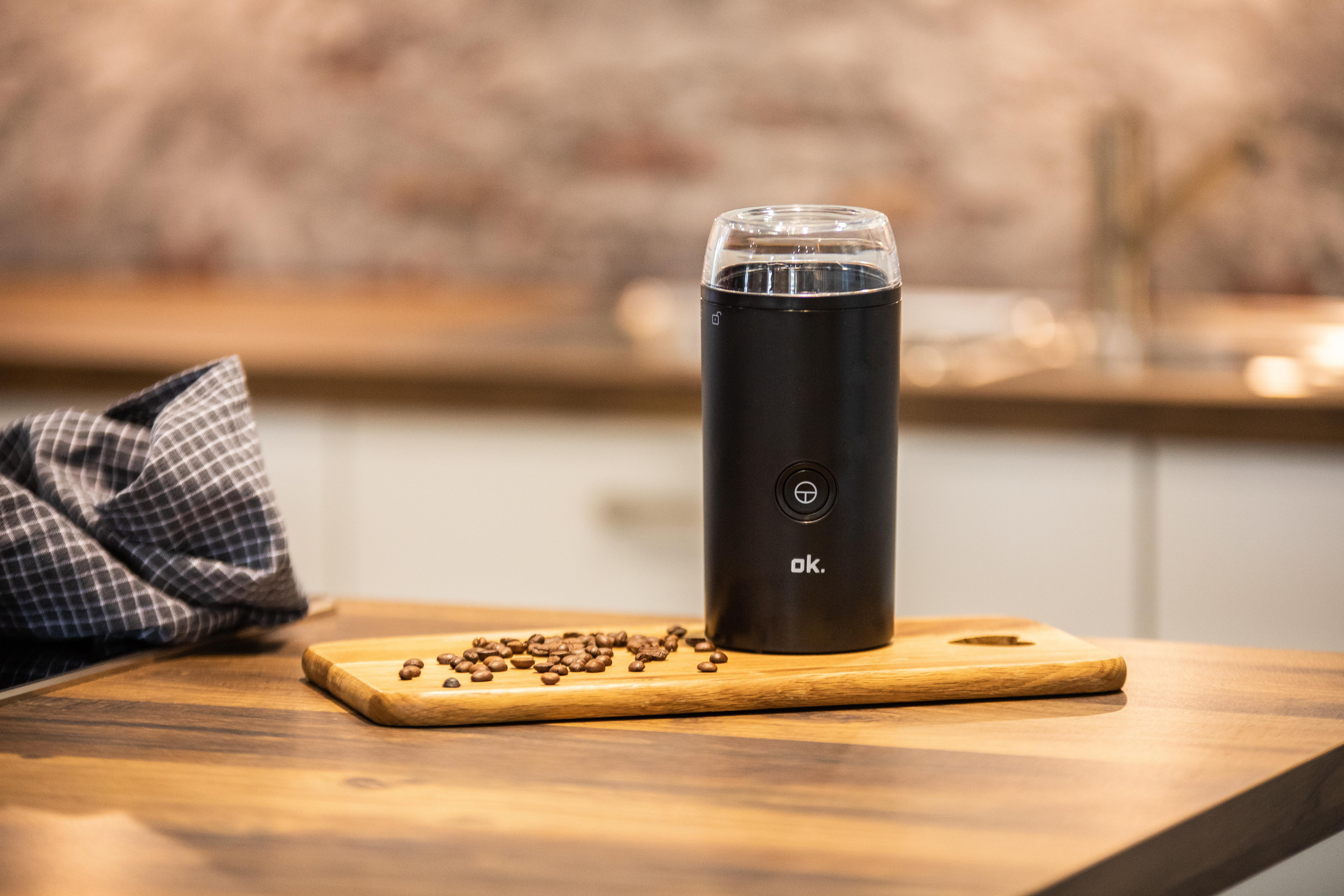 Schwarze Kaffeemühle, Kaffeebohnen und Holzschneidebrett auf einem Holztisch.