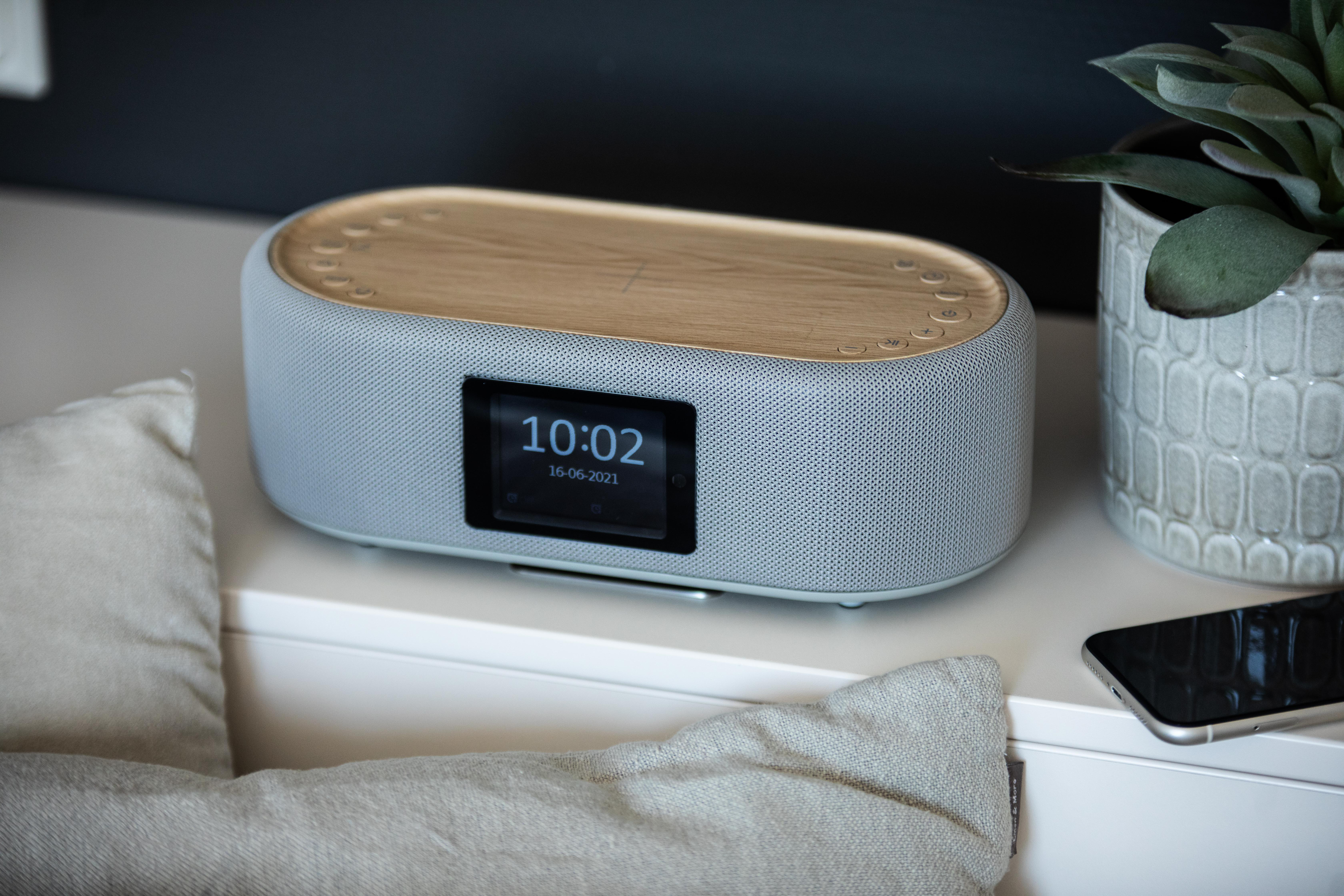 Grauer Lautsprecher mit Holzoberteil und Digitaluhr.