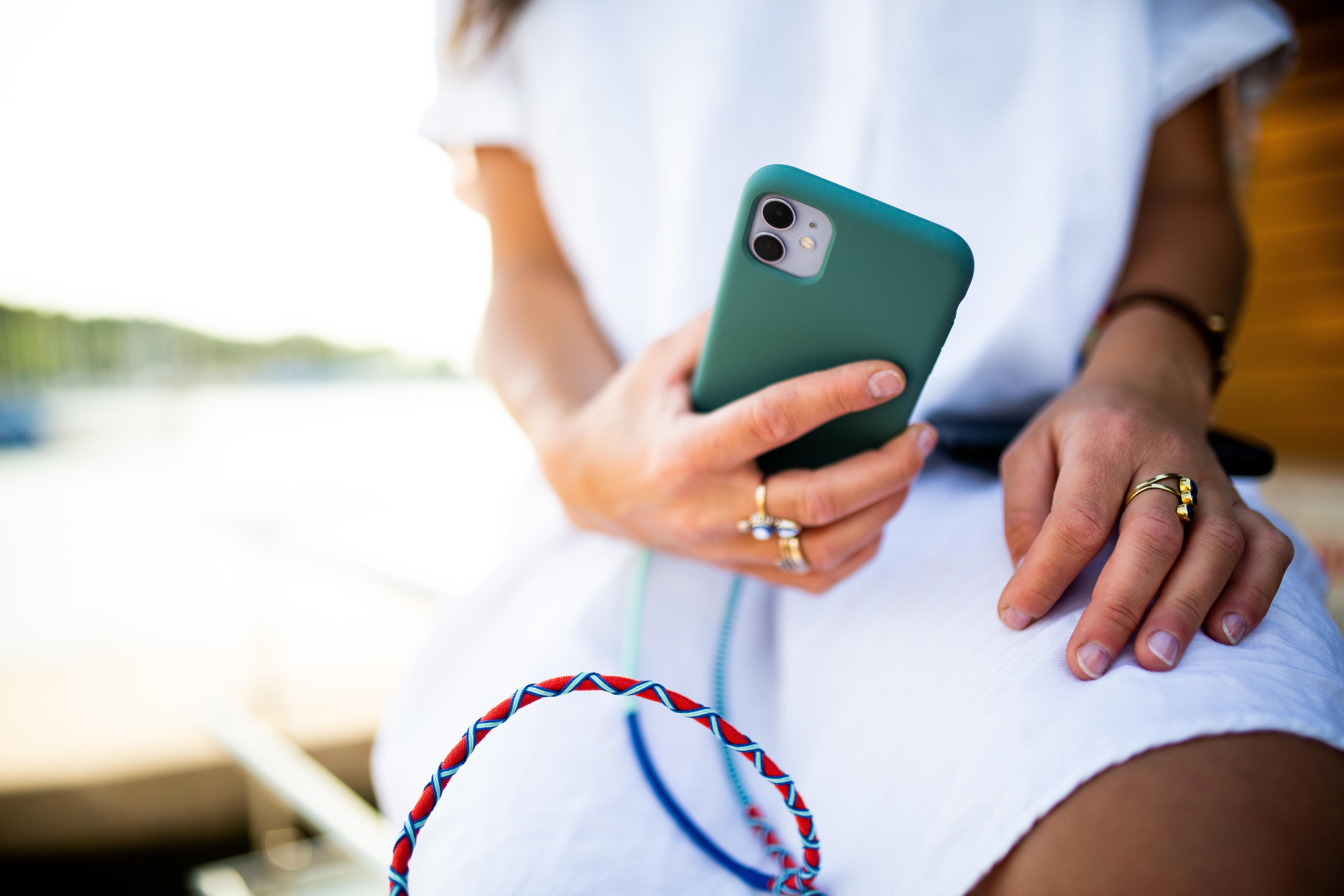 Frau hält grünes Telefon mit Hülle. Ihre Hände haben Ringe. Blaues und rotes Kabel.