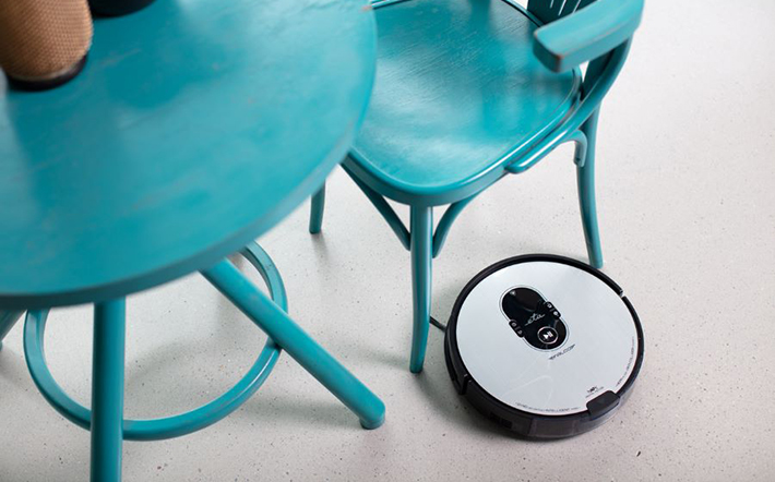 Egy robotporszívó egy türkiz asztal és szék közelében.