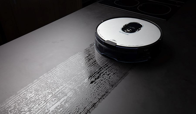 Egy robot porszívó sötét felületet tisztít, egy modern kinézetű konyhában.