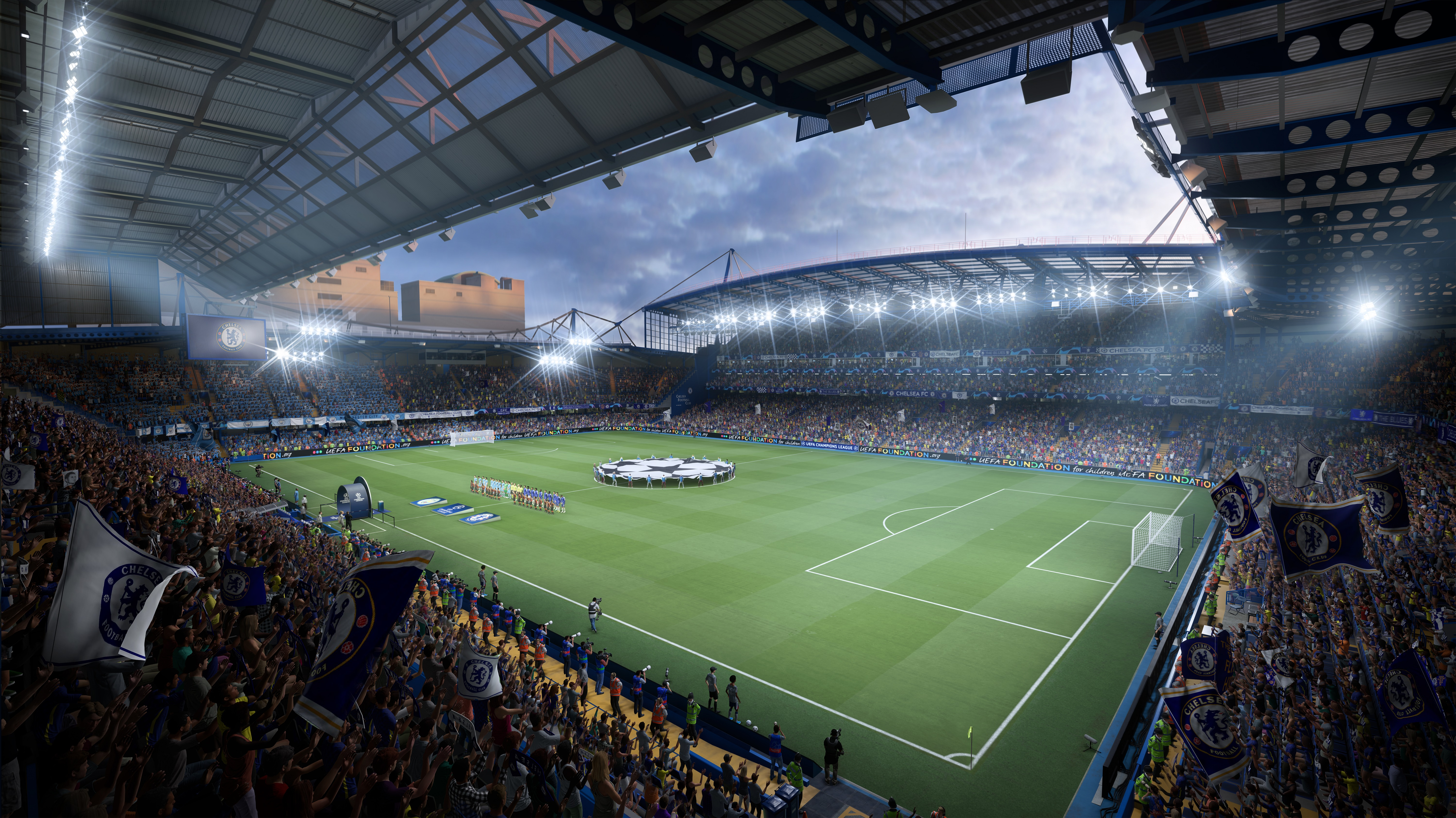 Een voetbalstadion vol fans, lichten en een groen veld. Vlaggen zijn zichtbaar.