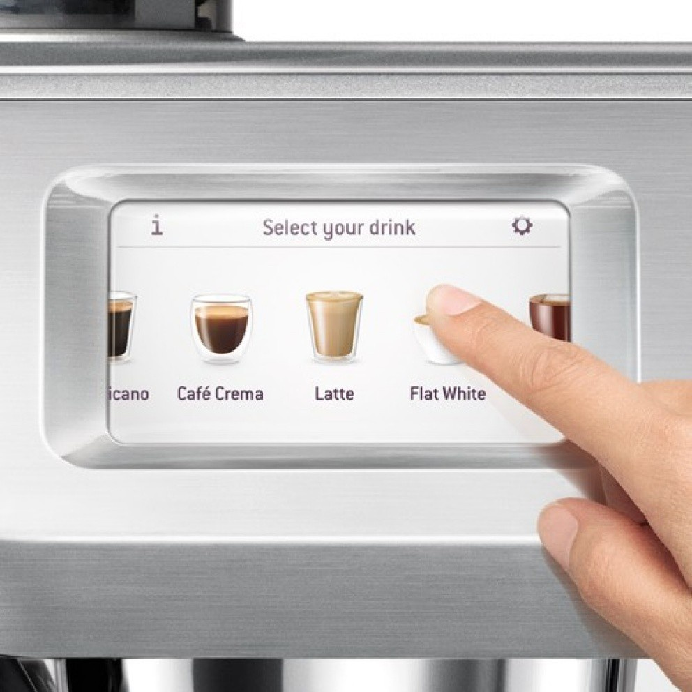 Une main touche l'option 'Flat White' sur l'écran tactile d'une machine à café. L'écran affiche différents choix de café : Icano, Café Crema, Latte.