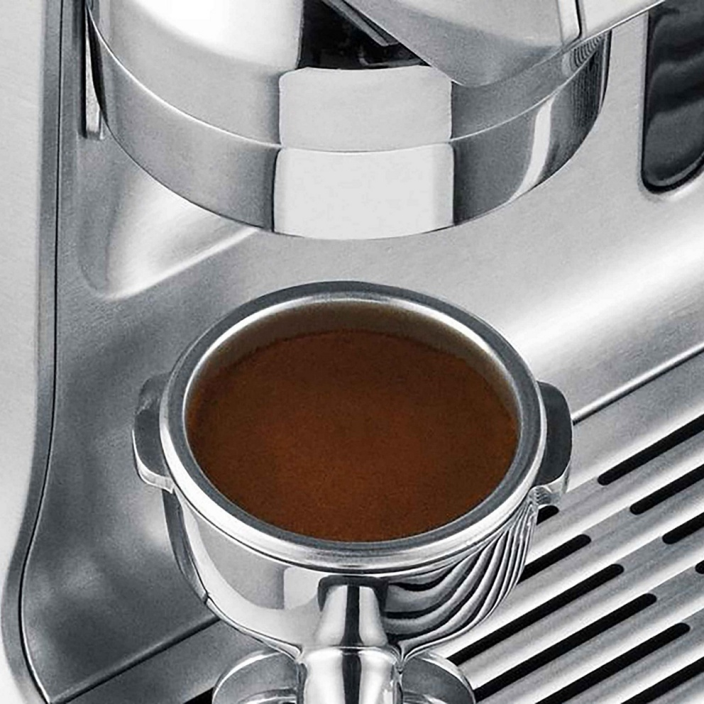 Gros plan sur une machine à expresso. Le porte-filtre est rempli de café et l'expresso est en cours d'extraction. Corps en acier inoxydable.