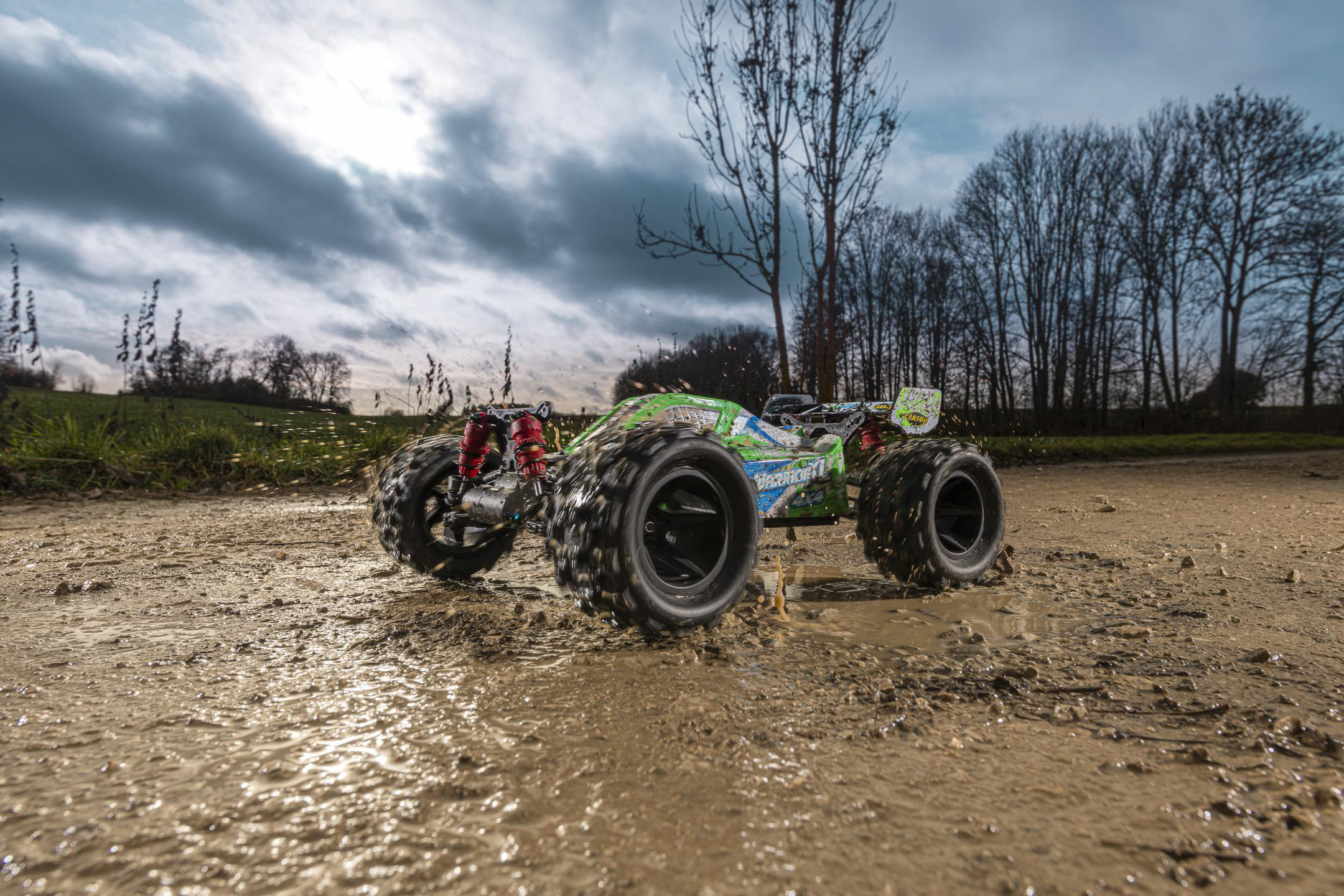 RC-Auto fährt in einer schlammigen Pfütze. Das Auto ist grün und schwarz. Wolkenhimmel im Hintergrund.
