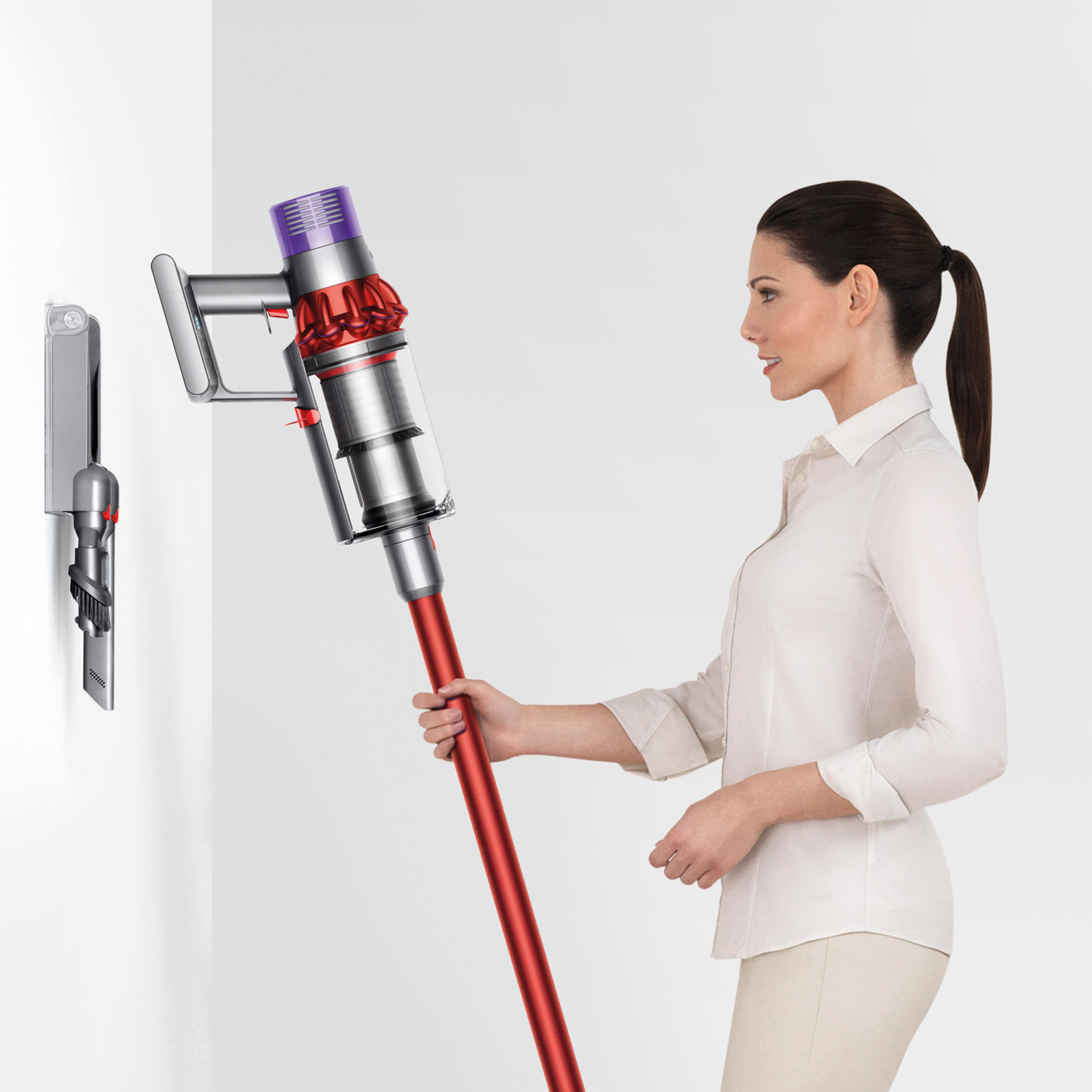Eine Frau, die einen rot-silbernen Staubsauger in der Nähe einer Wand hält.