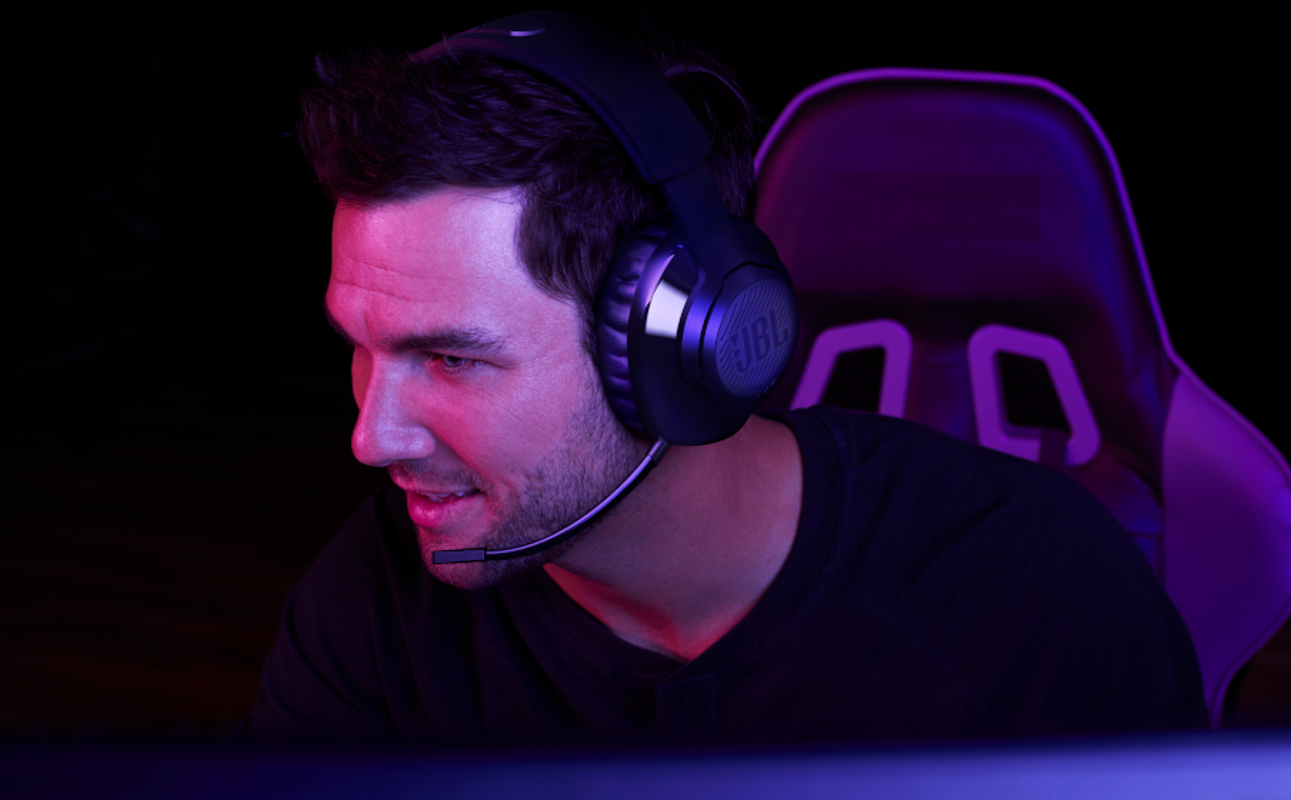 Ein Mann mit Gaming-Headset und Mikrofon sitzt vor einem Bildschirm, der in violetten Farbtönen beleuchtet wird.