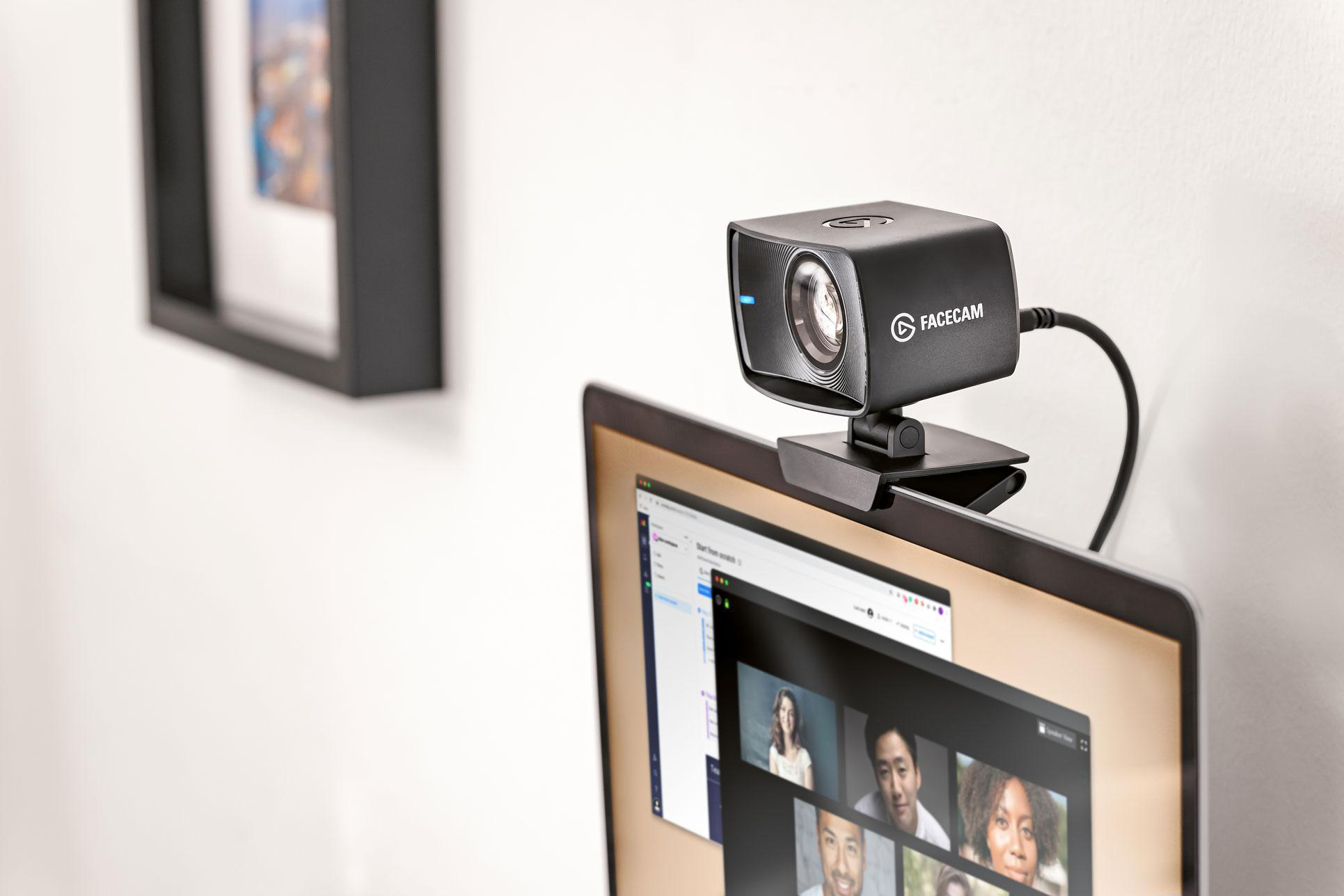 Eine schwarze Webcam, die an einem Laptop befestigt ist. Der Laptop zeigt einen Videoanruf mit mehreren Teilnehmern.