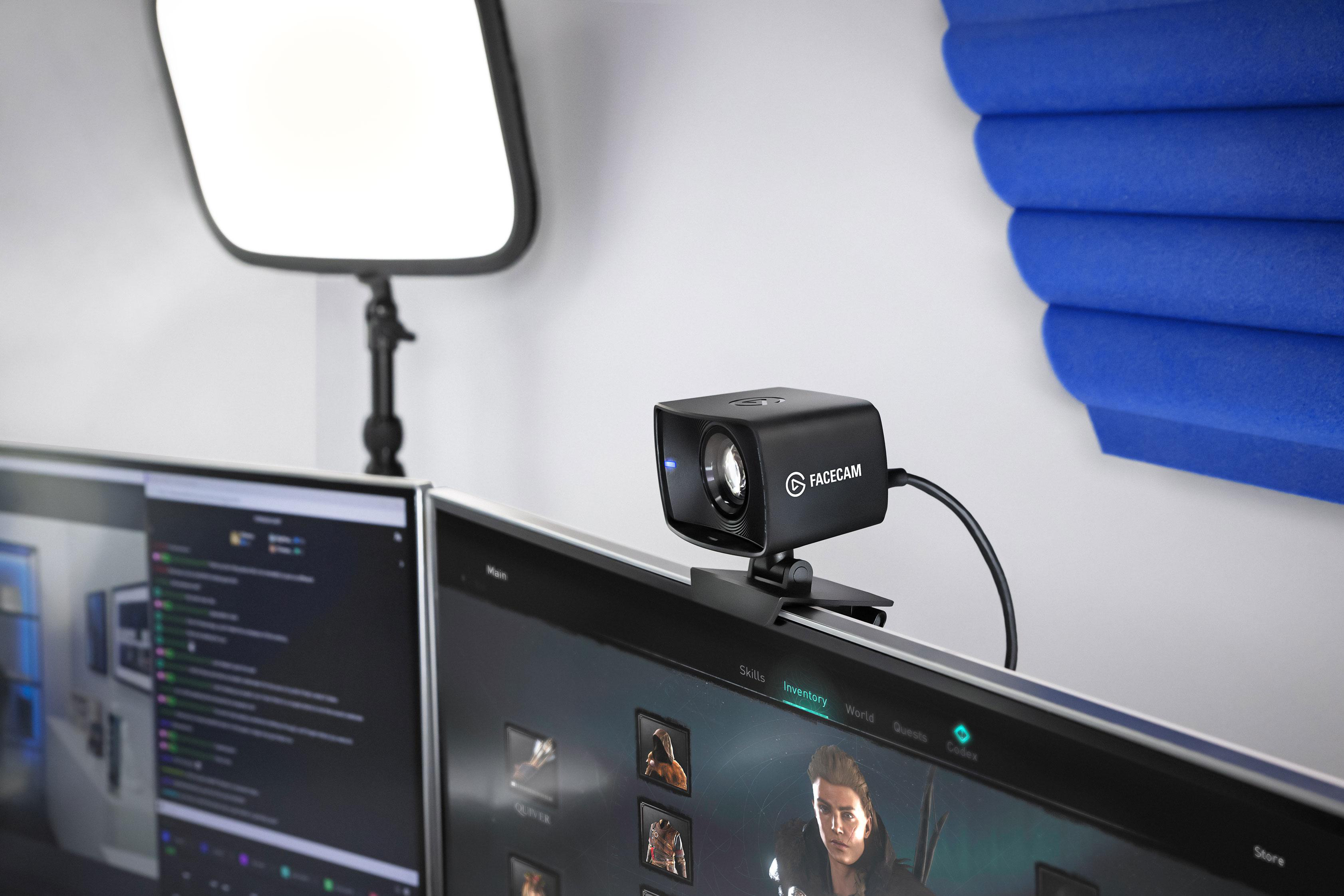 Schwarze Webcam auf Monitor, zwei Monitore im Hintergrund.