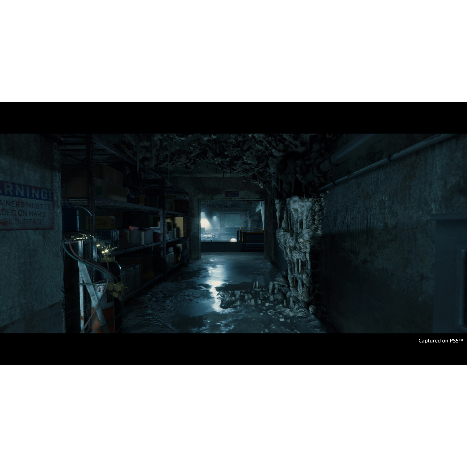 Interior oscuro y arenoso de un edificio, con suelo mojado y pasillo mal iluminado.