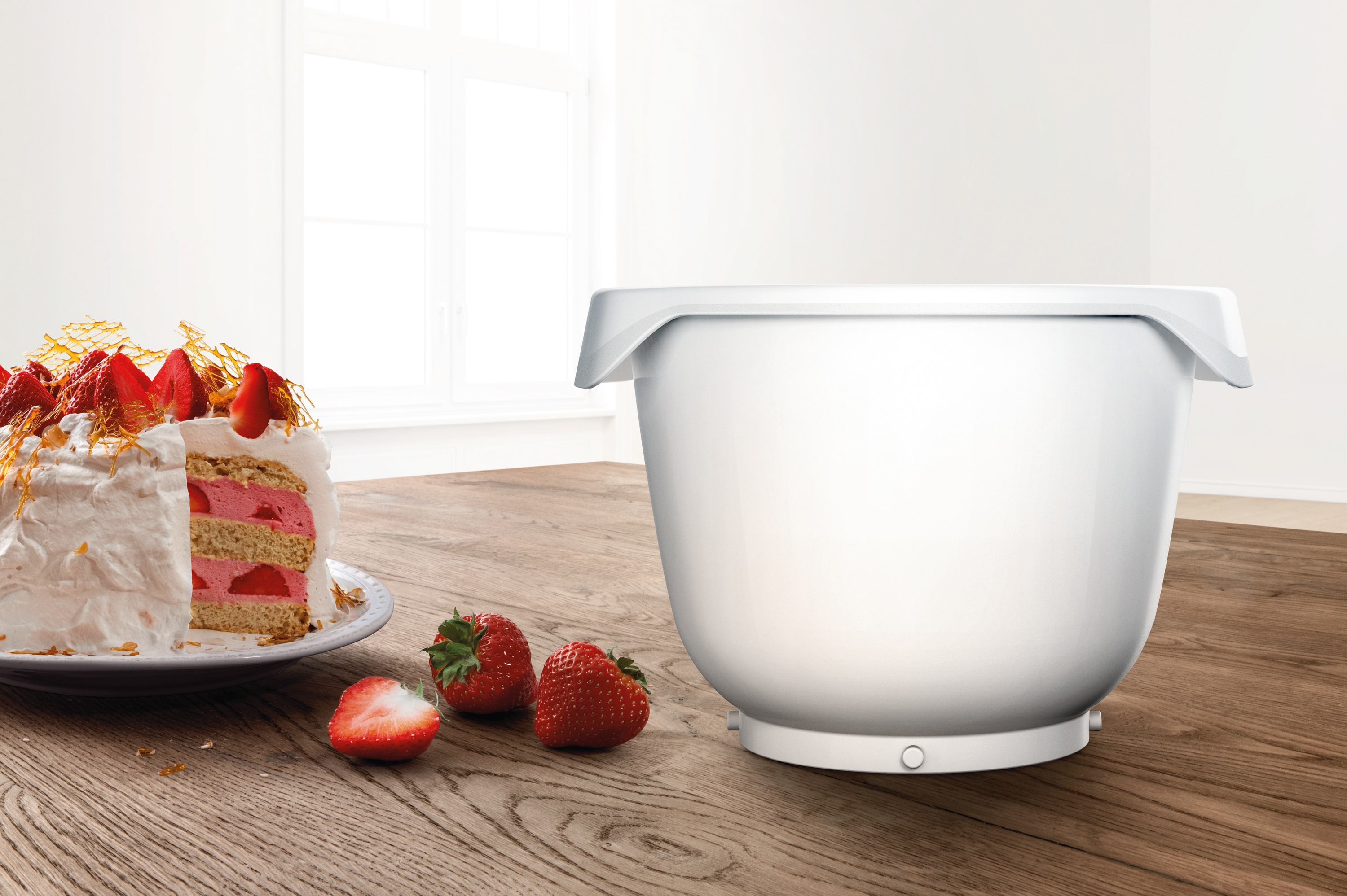 Eine weiße Schüssel neben einem Kuchen mit Erdbeeren und ein paar Erdbeeren auf einem Holztisch.