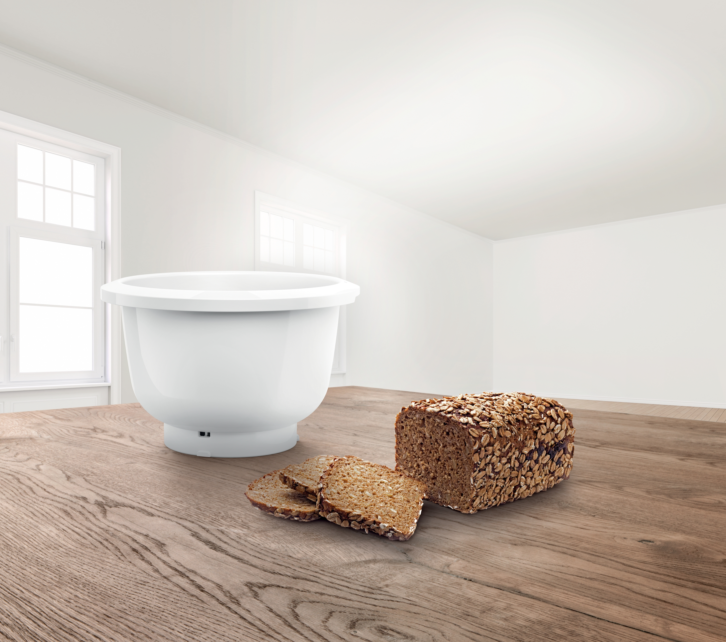 Weiße Rührschüssel neben einem Brotlaib und Scheiben auf einem Holztisch, heller Raum.