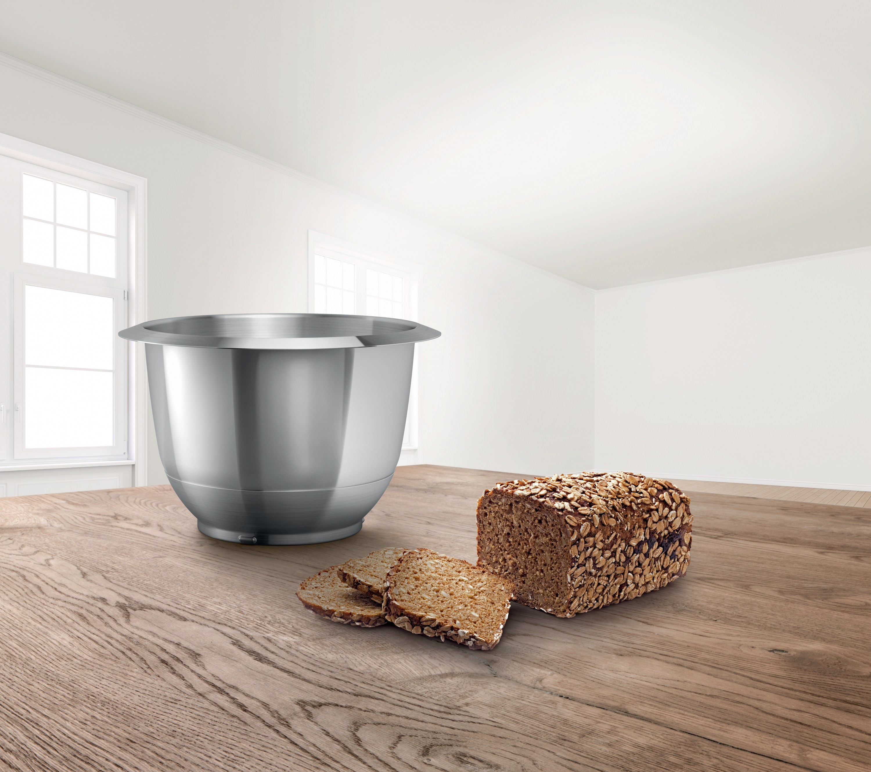 Eine Edelstahl-Rührschüssel neben einem Brotlaib mit Samen und drei Brotscheiben.