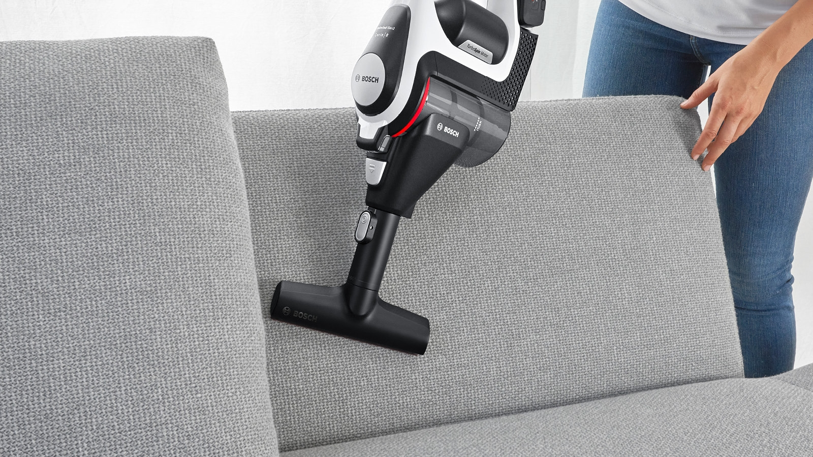 Frau benutzt Bosch Staubsauger auf einem Sofa.