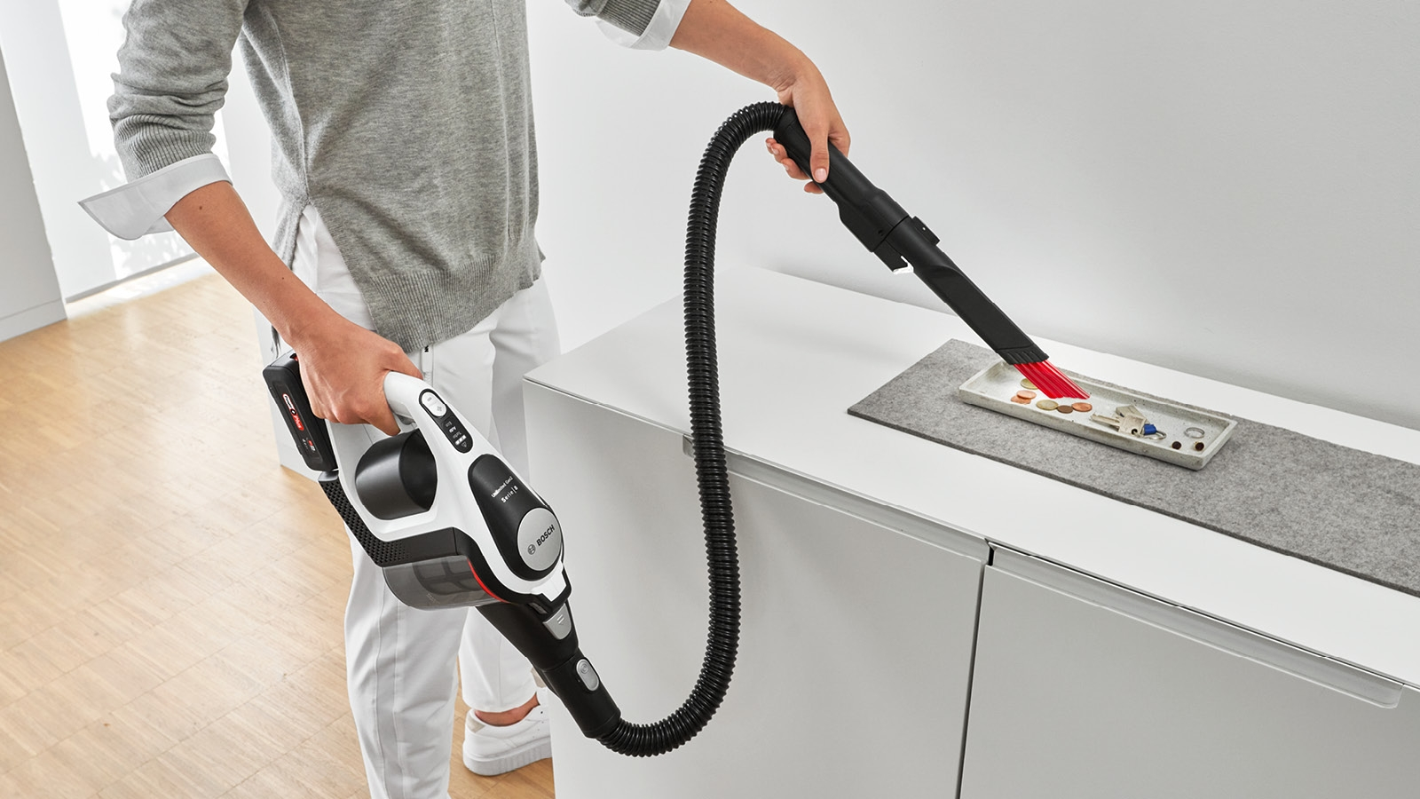 Eine Person saugt eine weiße Oberfläche mit einem kabellosen Staubsauger ab.