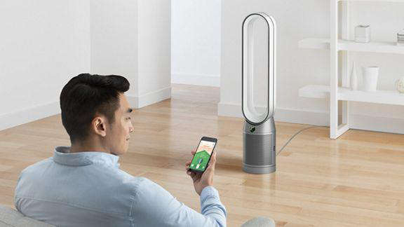Ein Mann, der ein Smartphone benutzt, um einen Dyson-Ventilator in einer modernen Inneneinstellung zu steuern.