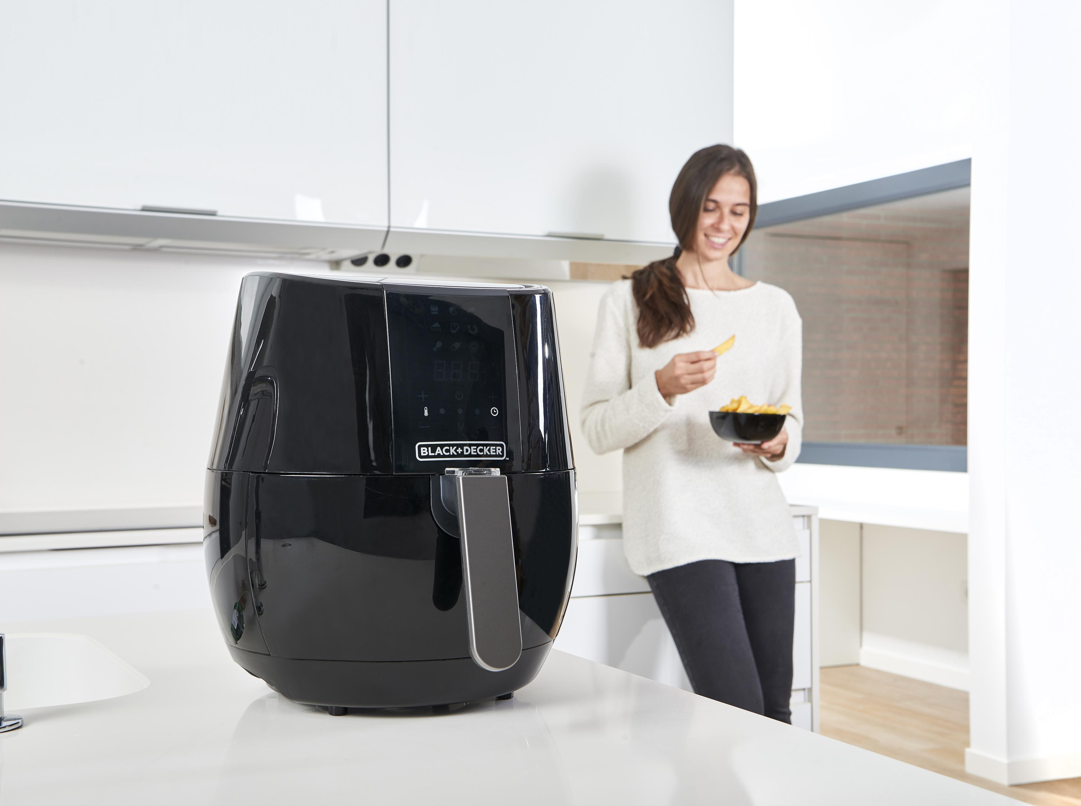 Black and Decker Heißluftfritteuse auf weißer Arbeitsplatte, Frau mit Pommes im Hintergrund.