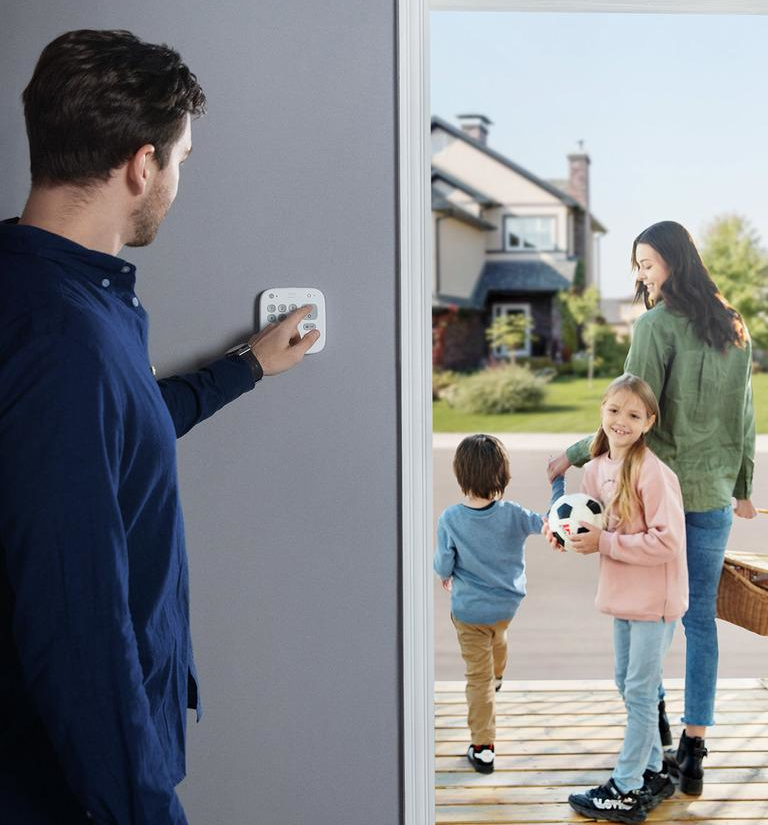 A man is using a keypad on a wall. A family is walking out of a door in the background.