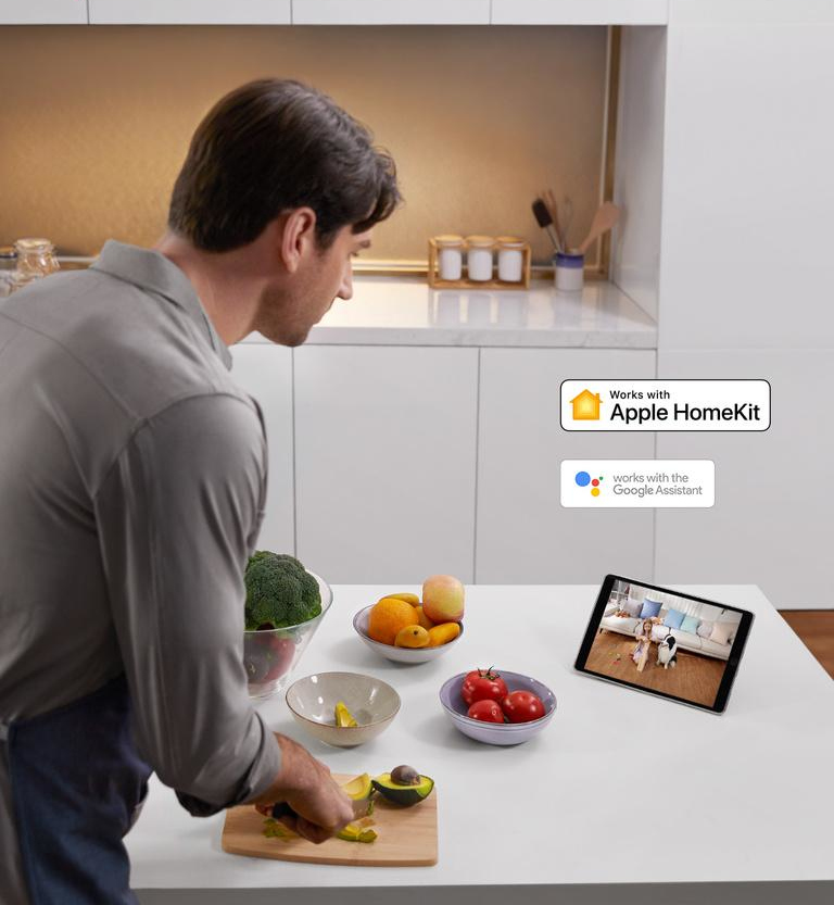 Man in de keuken maakt eten klaar, tablet toont livestream. Fruit en groenten op tafel.