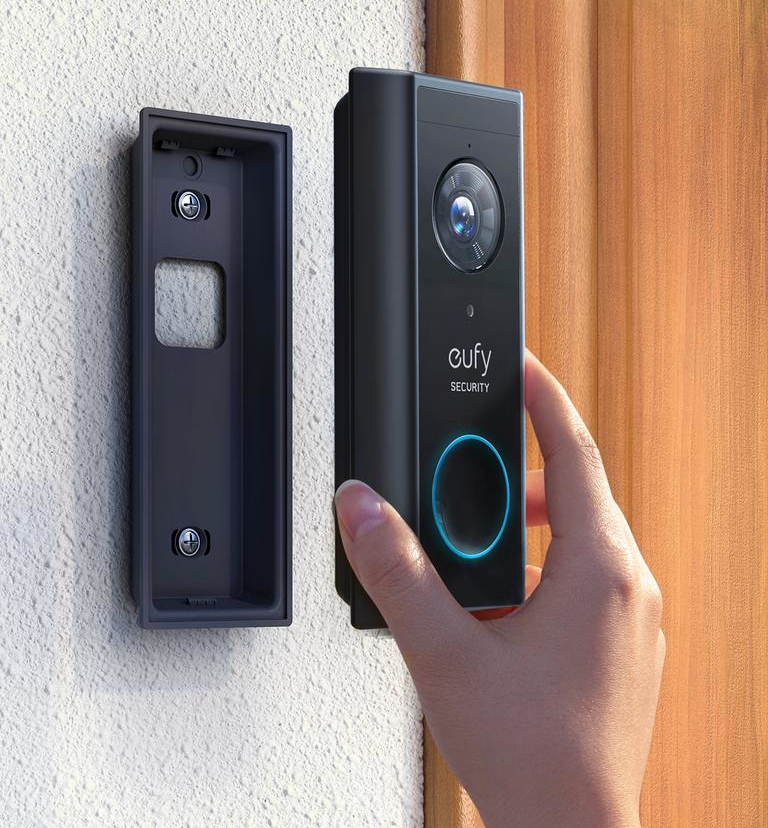 La main d'une personne installant une sonnette noire sur un mur, avec un support à proximité.