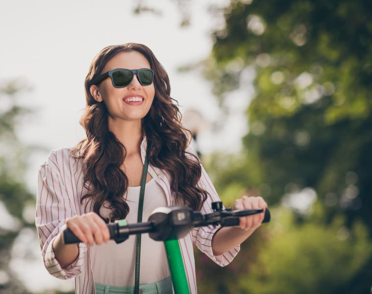Frau auf einem Roller mit Sonnenbrille, lächelnd.