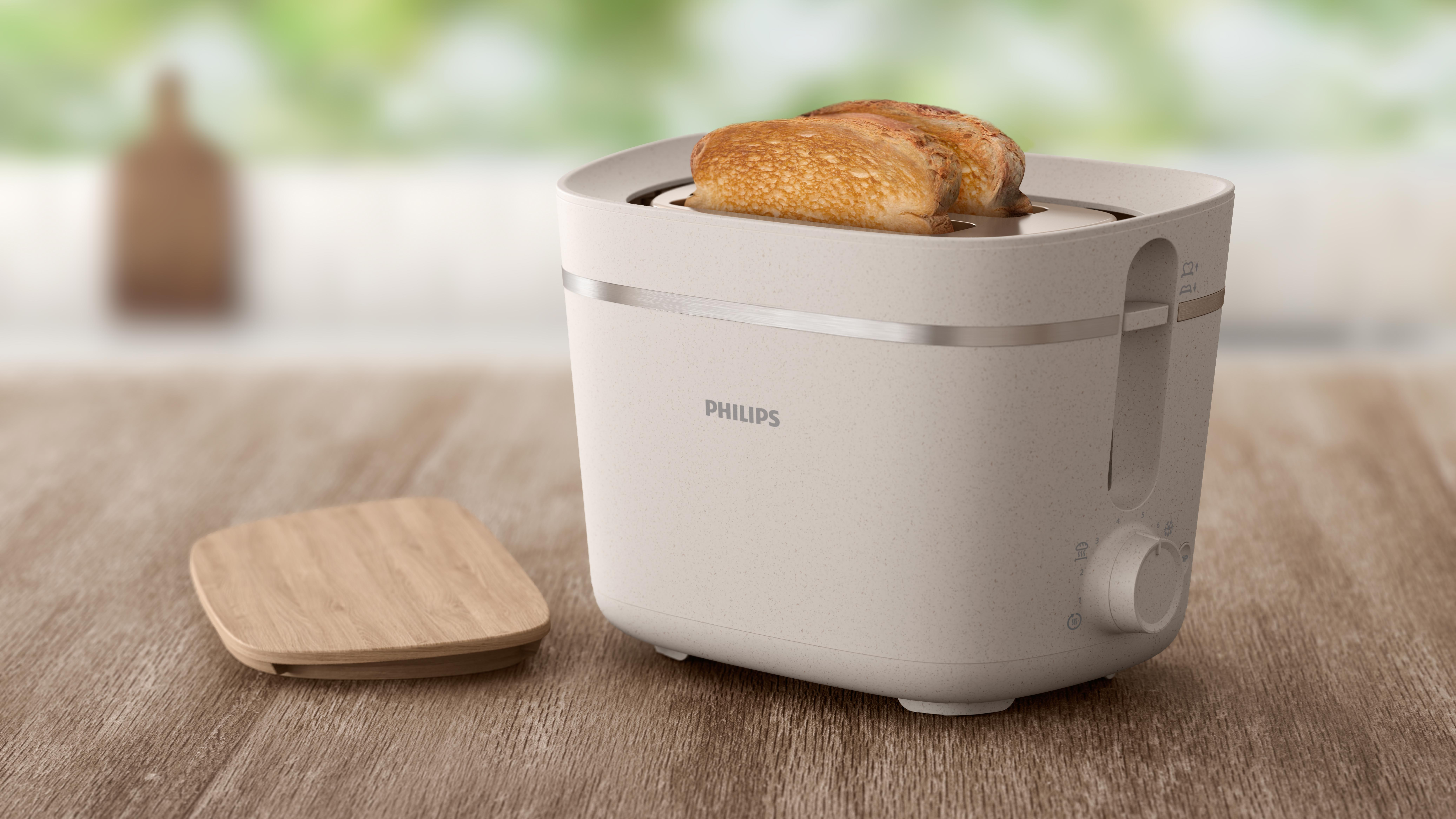Cremefarbener Toaster mit zwei Toastscheiben. Ein Holzdeckel liegt links.