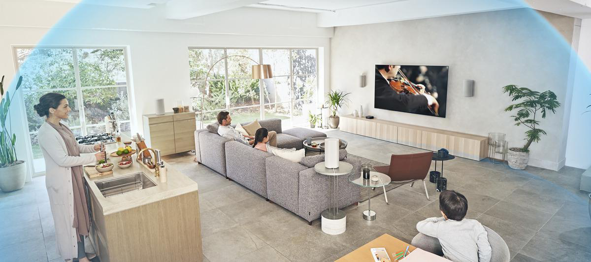 Wohnzimmer mit Fernseher, Familie und Smart Speaker auf einem Beistelltisch.