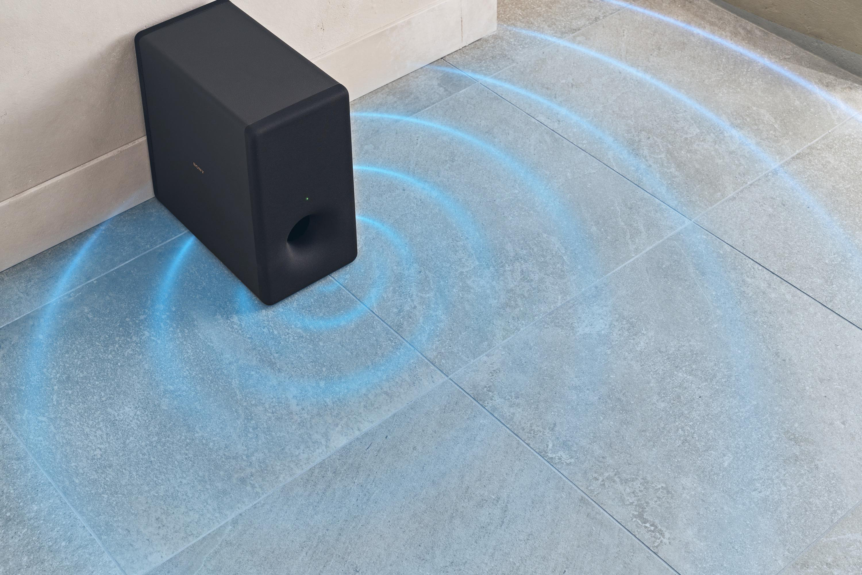 Ein schwarzer Subwoofer steht in der Nähe einer Ecke. Blaue Schallwellen gehen vom Lautsprecher aus.