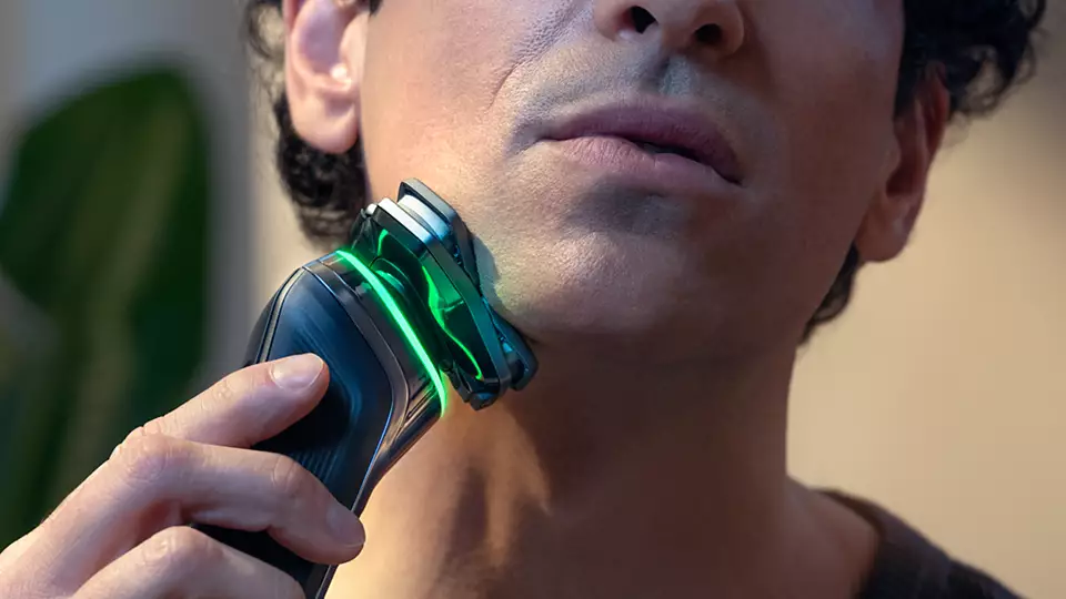 Ein Mann benutzt einen elektrischen Rasierer mit grünen Lichtdetails am Rasierer.