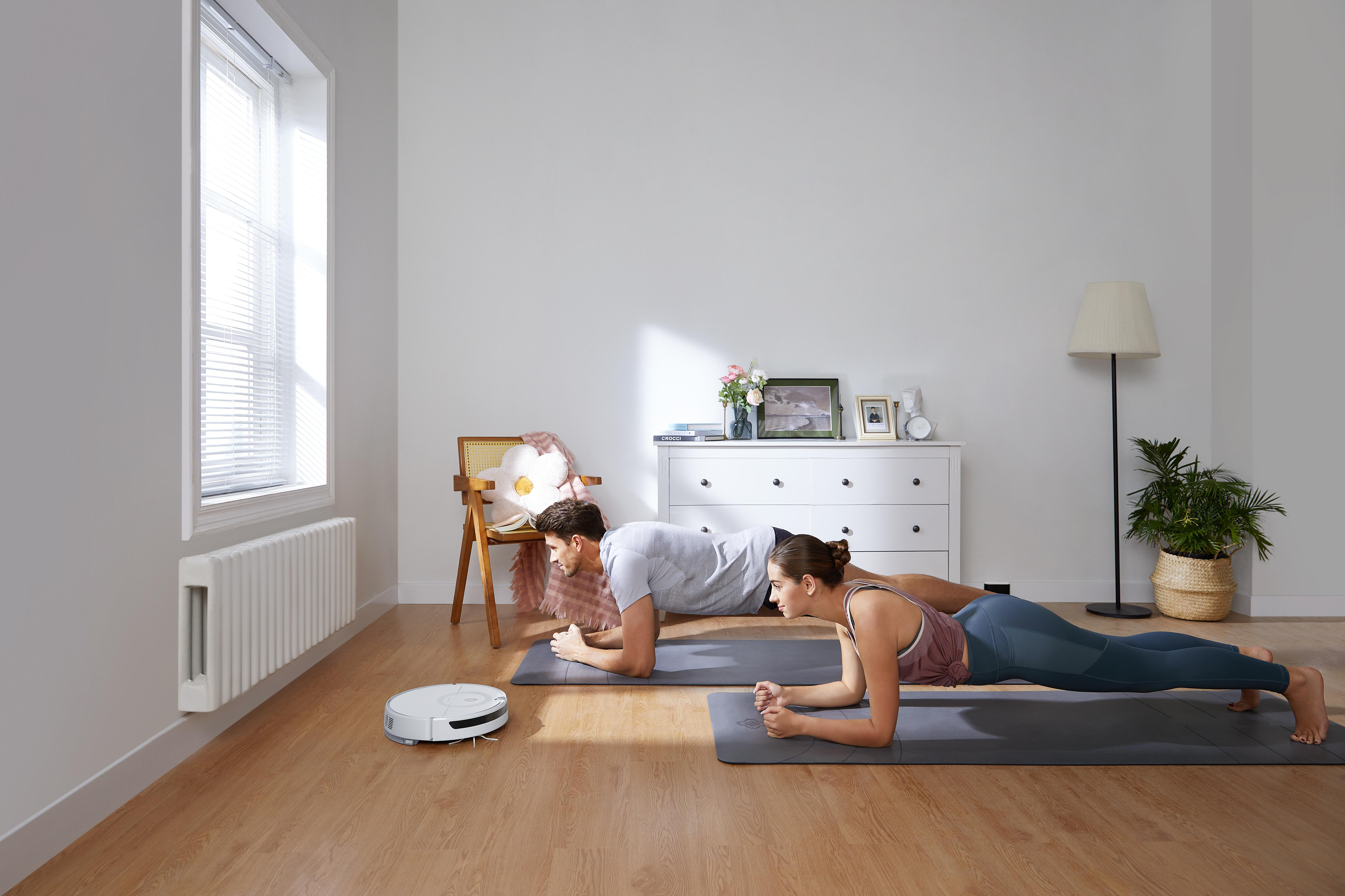 Ein Paar macht im Raum mit einem Roboterstaubsauger eine Plank-Übung.