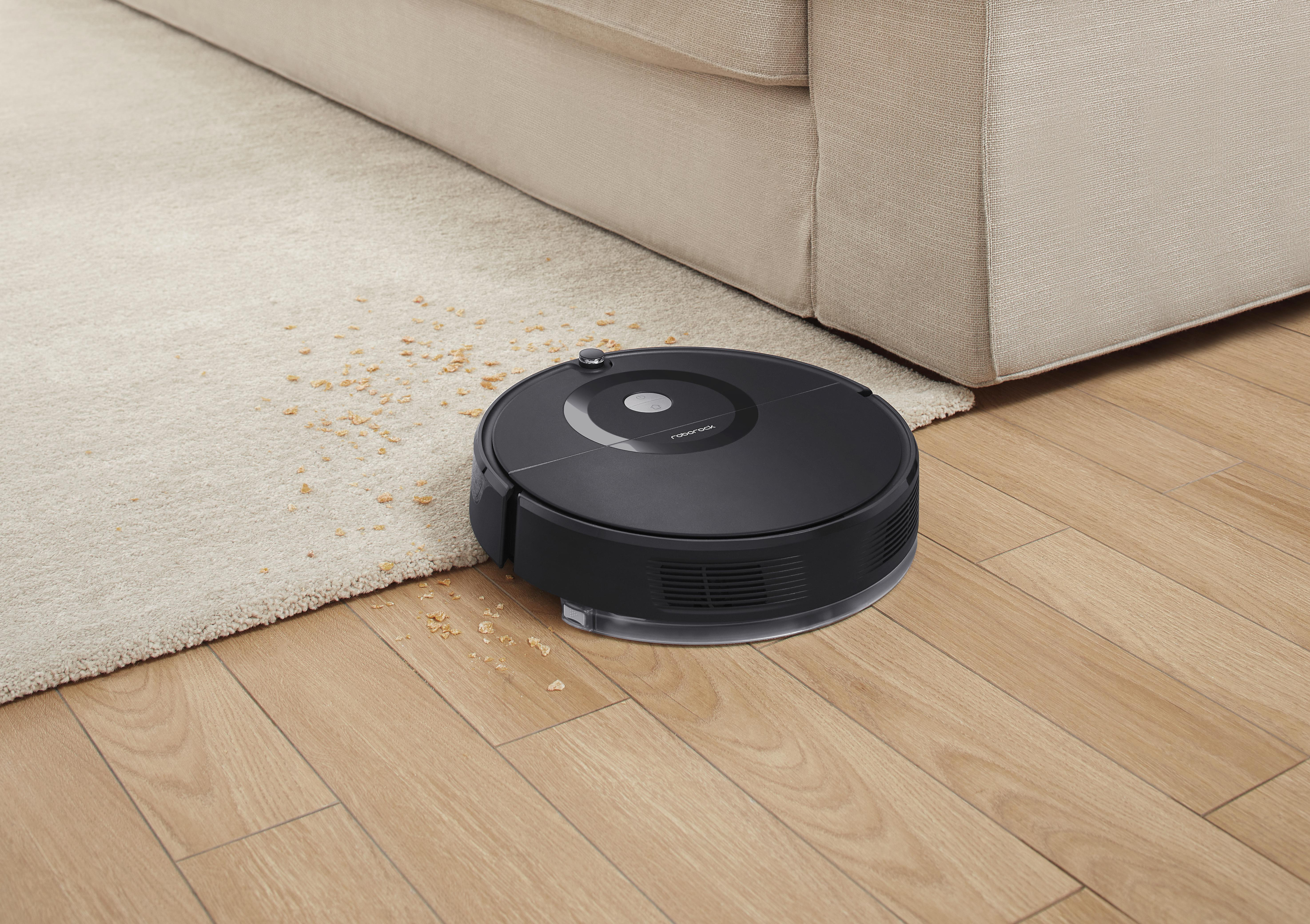 Schwarzer Roboter-Staubsauger auf Holzboden neben Teppich.