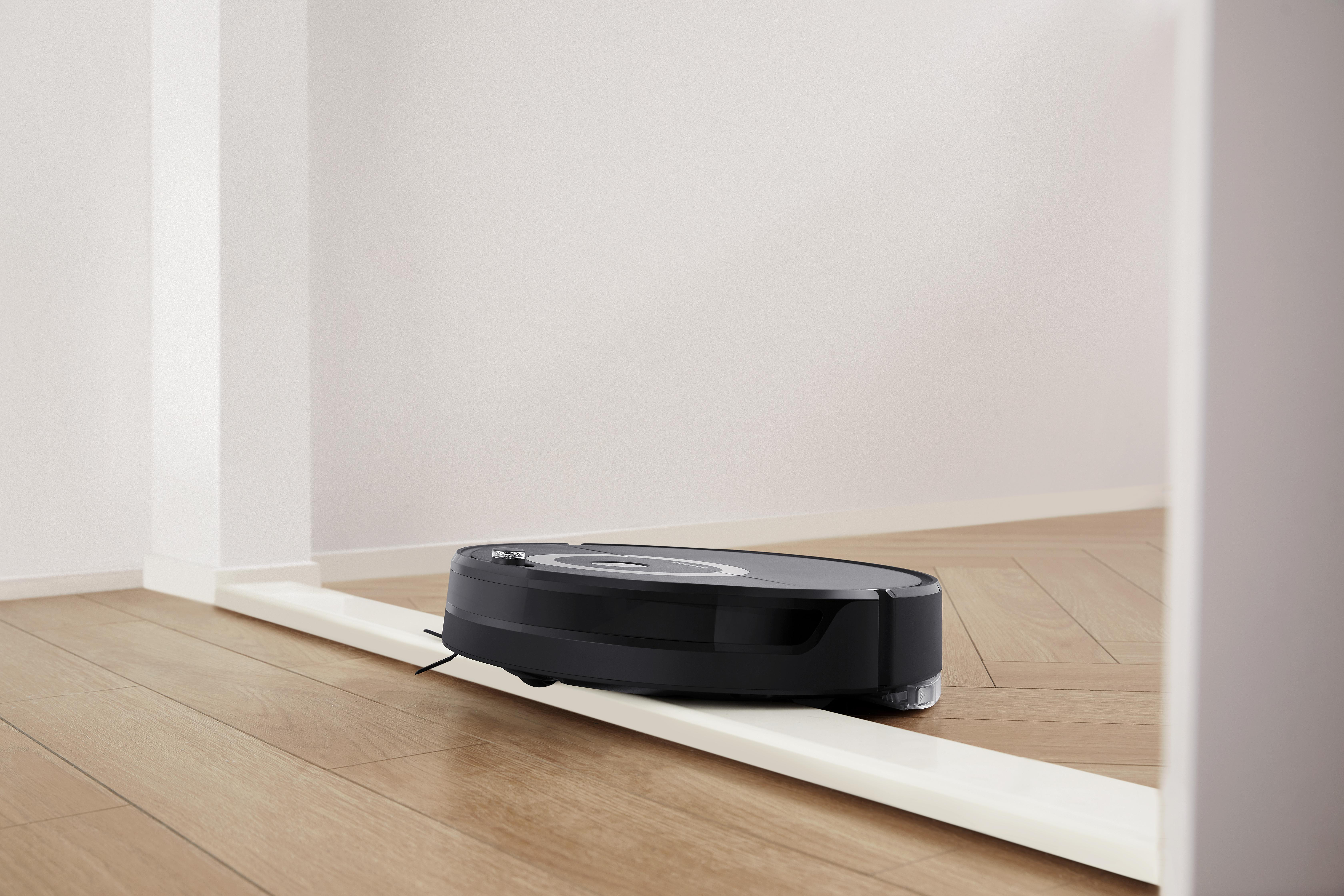 Schwarzer Roboter-Staubsauger auf Holzboden, der durch eine Tür geht.