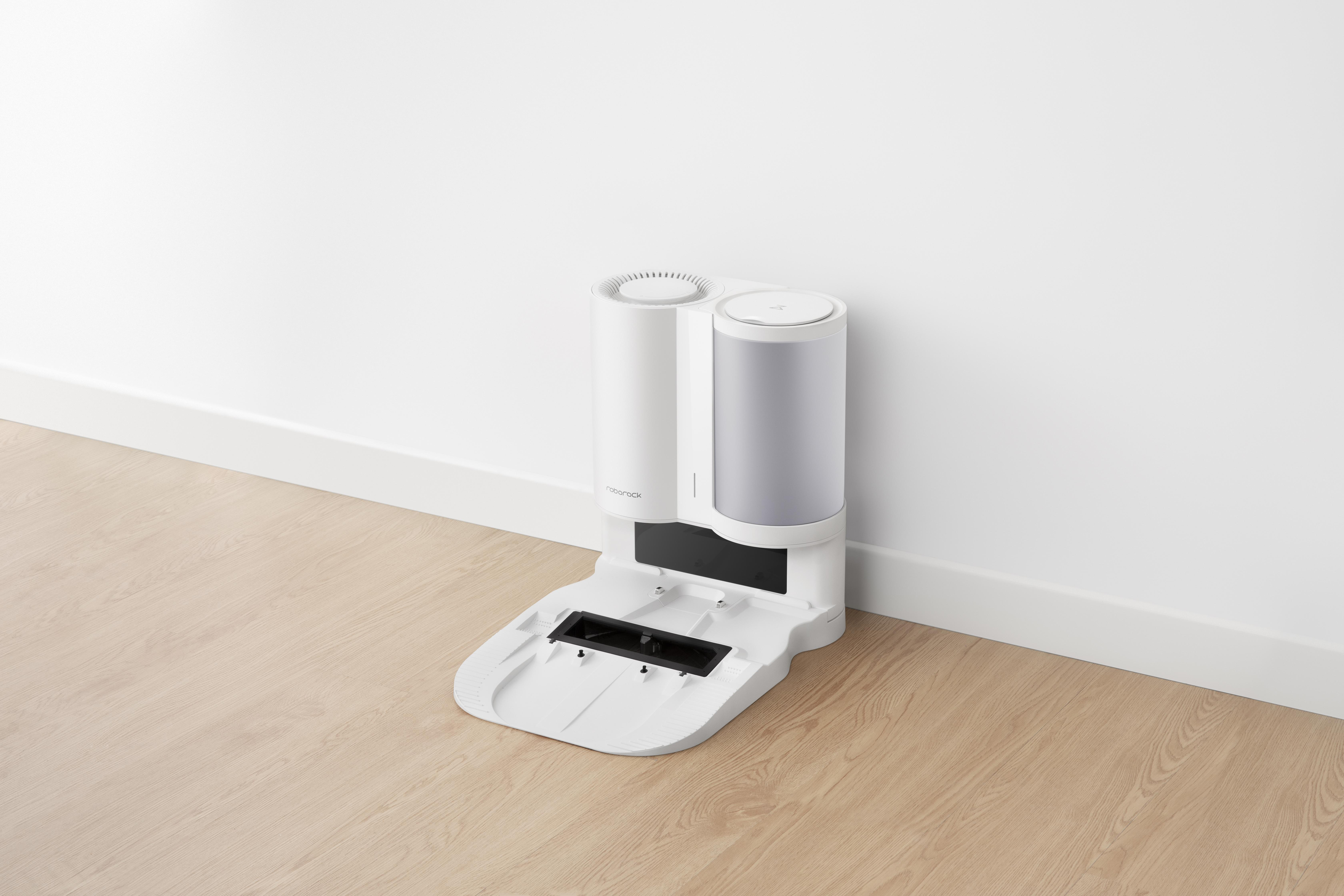 Weiße Roboter-Staubsauger-Basisstation. Zwei zylindrische Teile oben, eine flache Basis, auf Holzboden.
