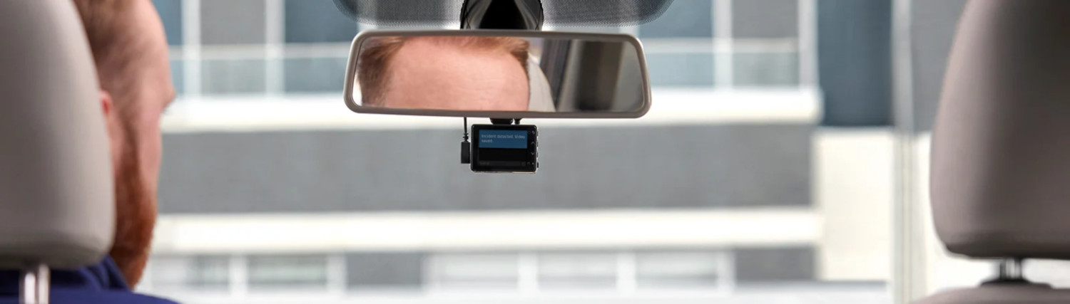 Vue du rétroviseur à l'intérieur d'une voiture ; reflet d'un homme et d'une dashcam.