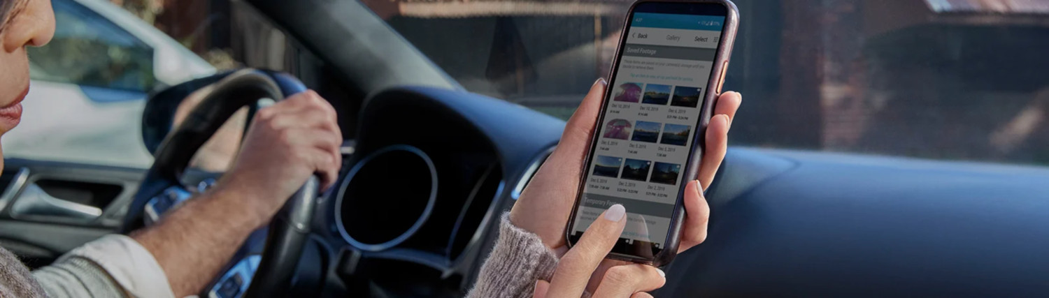 Een persoon houdt een smartphone vast tijdens het rijden. De telefoon toont een interface van een dashcam-app.