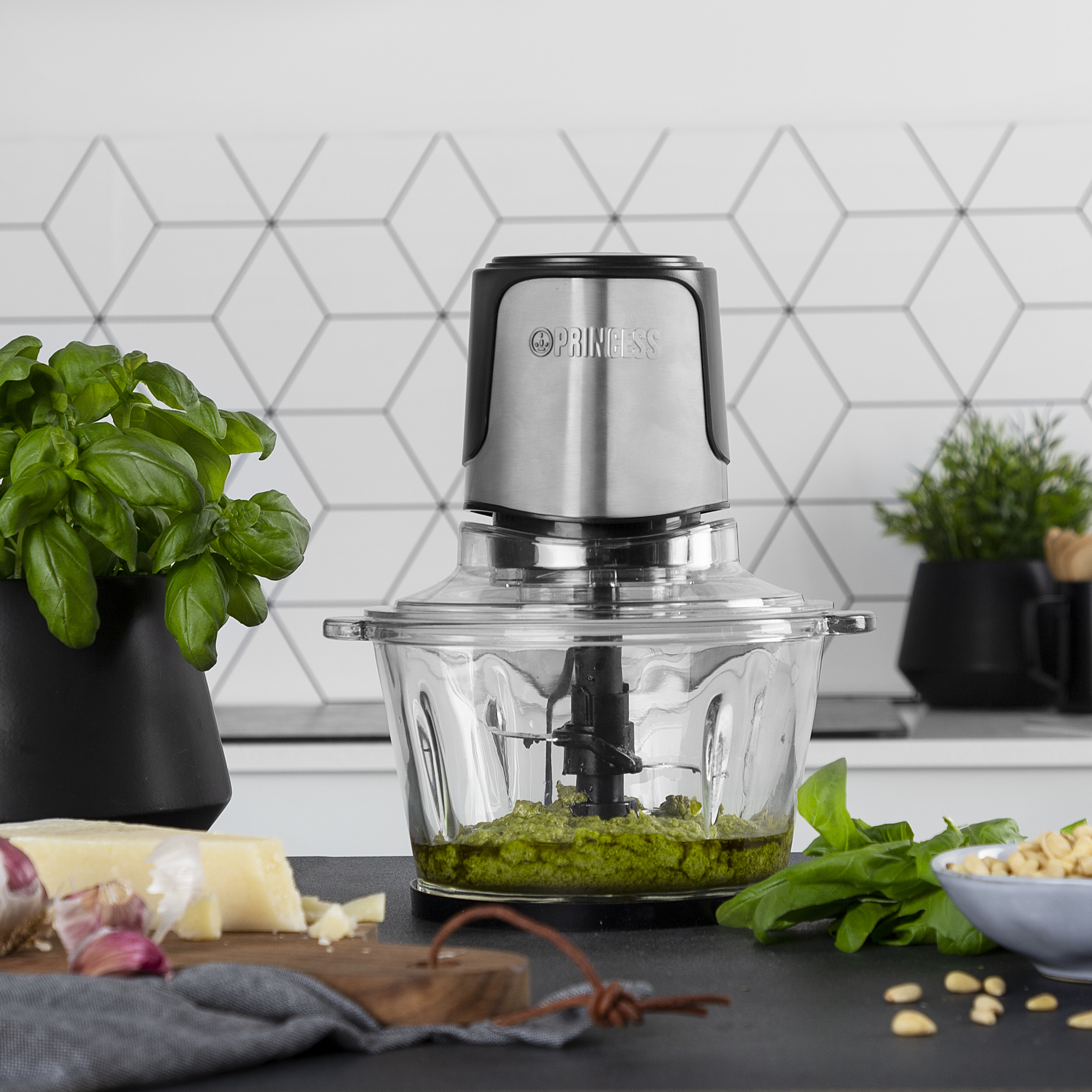 Keukenmachine die pesto hakt, met ingrediënten als basilicum, kaas en noten in de buurt.