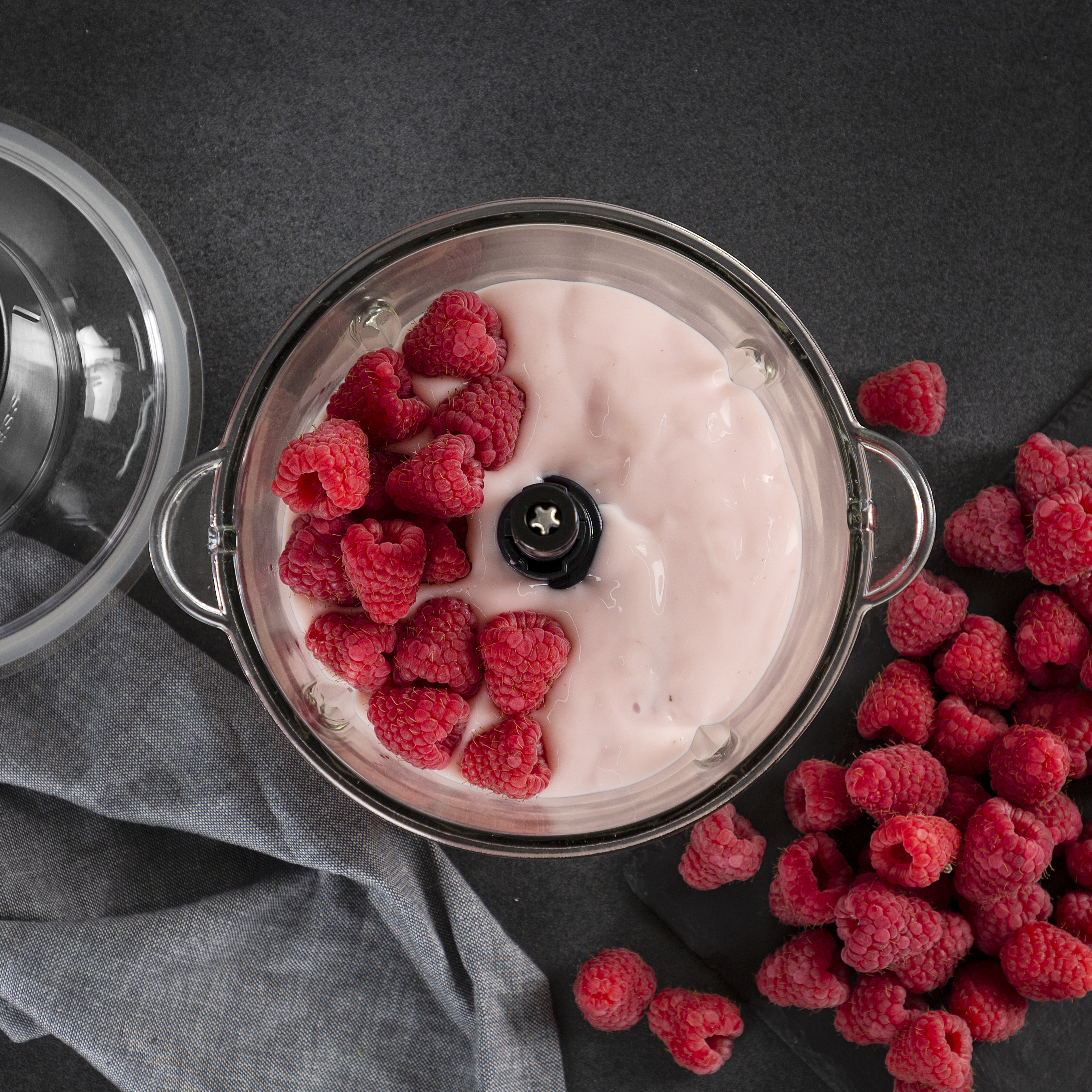 Blender met roze crème en frambozen in een glazen container en frambozen eromheen.