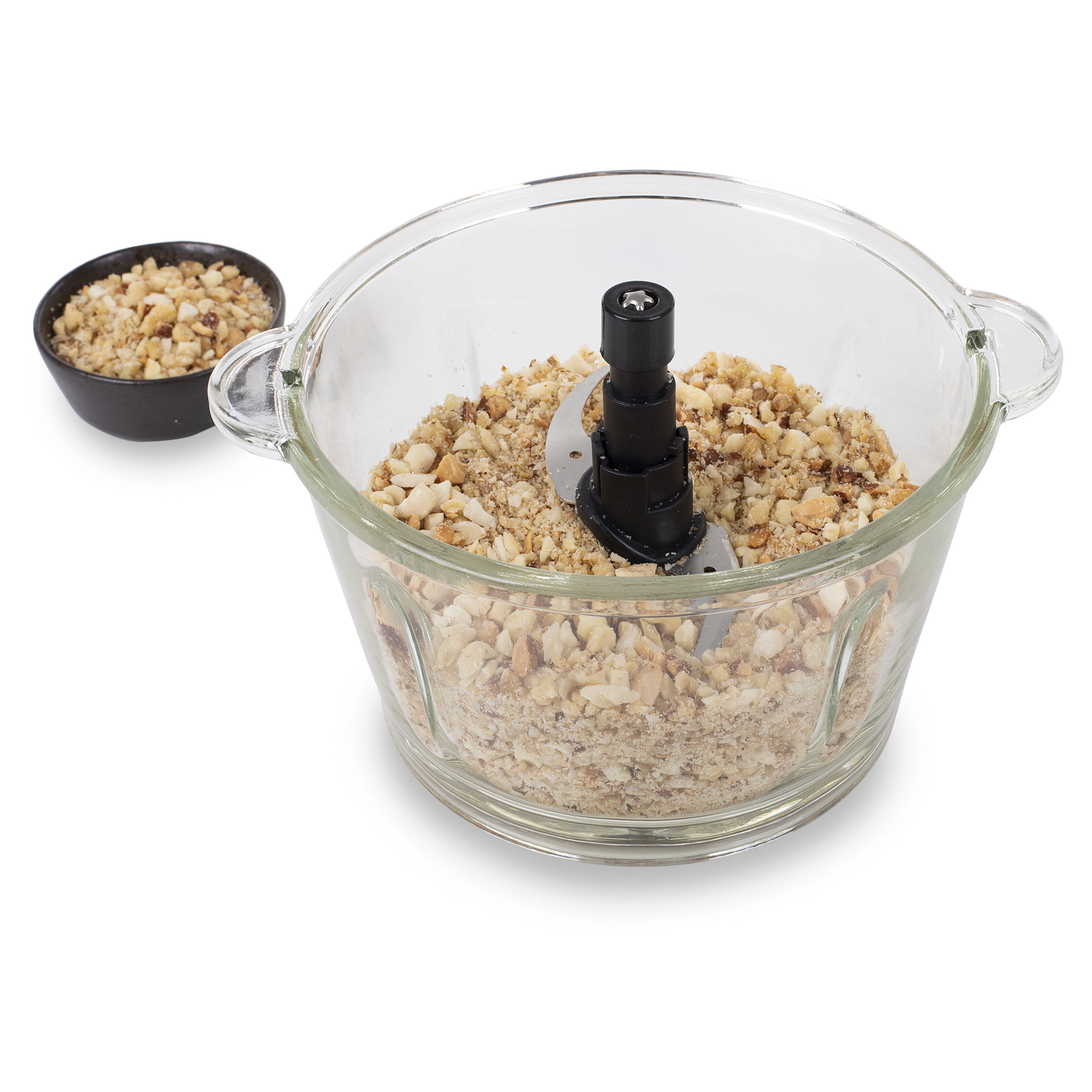 Een doorzichtige foodprocessor met gehakte noten, met een zwarte kom noten ernaast op een witte ondergrond.