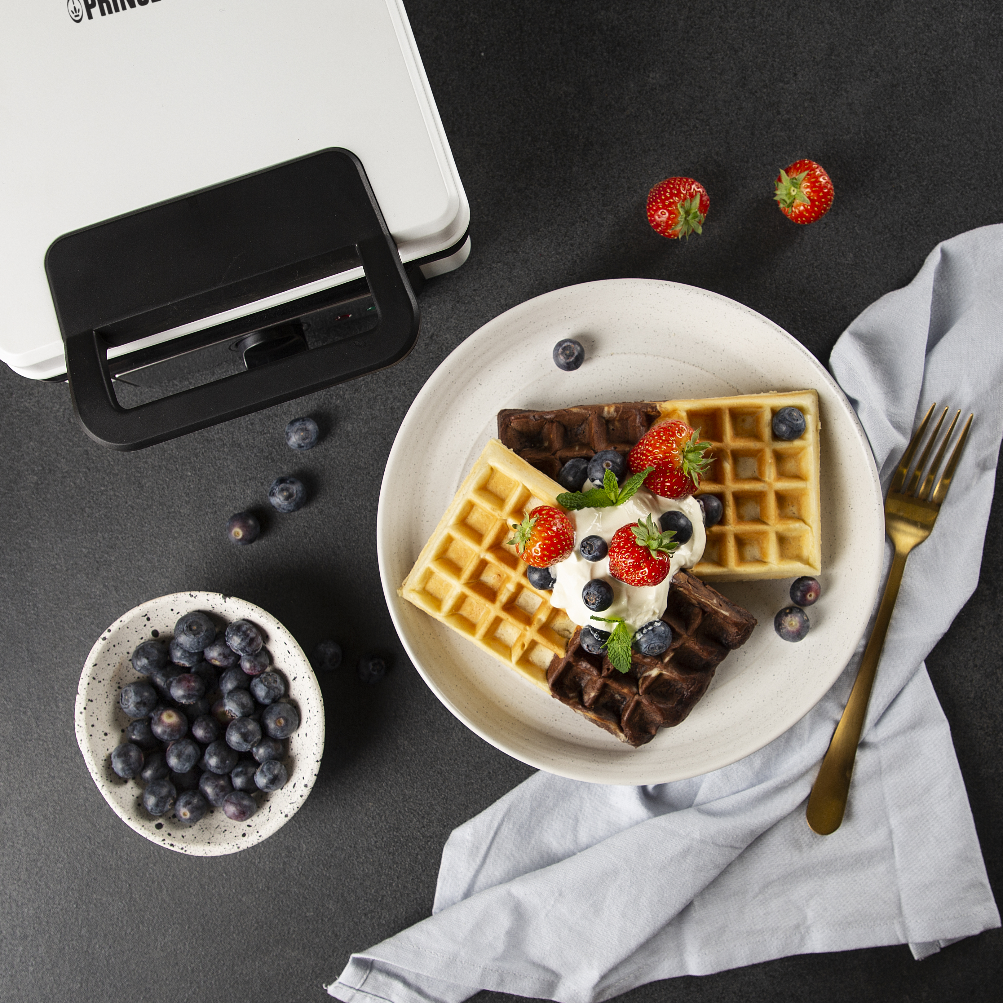Wafels op een bord met blauwe bessen, aardbeien en room, met een vork.