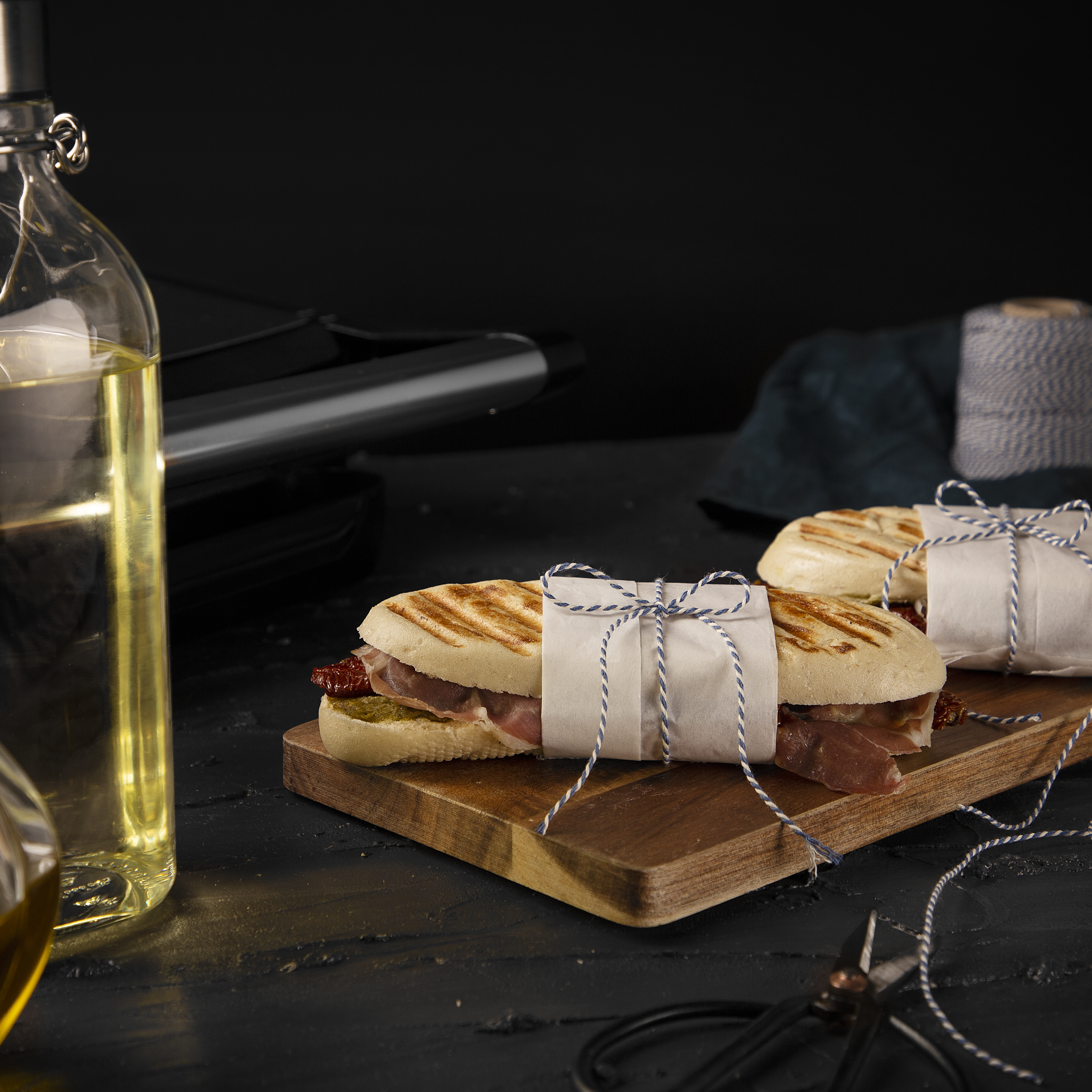Sandwiches wrapped in paper on a wooden board, oil bottle on the side.
