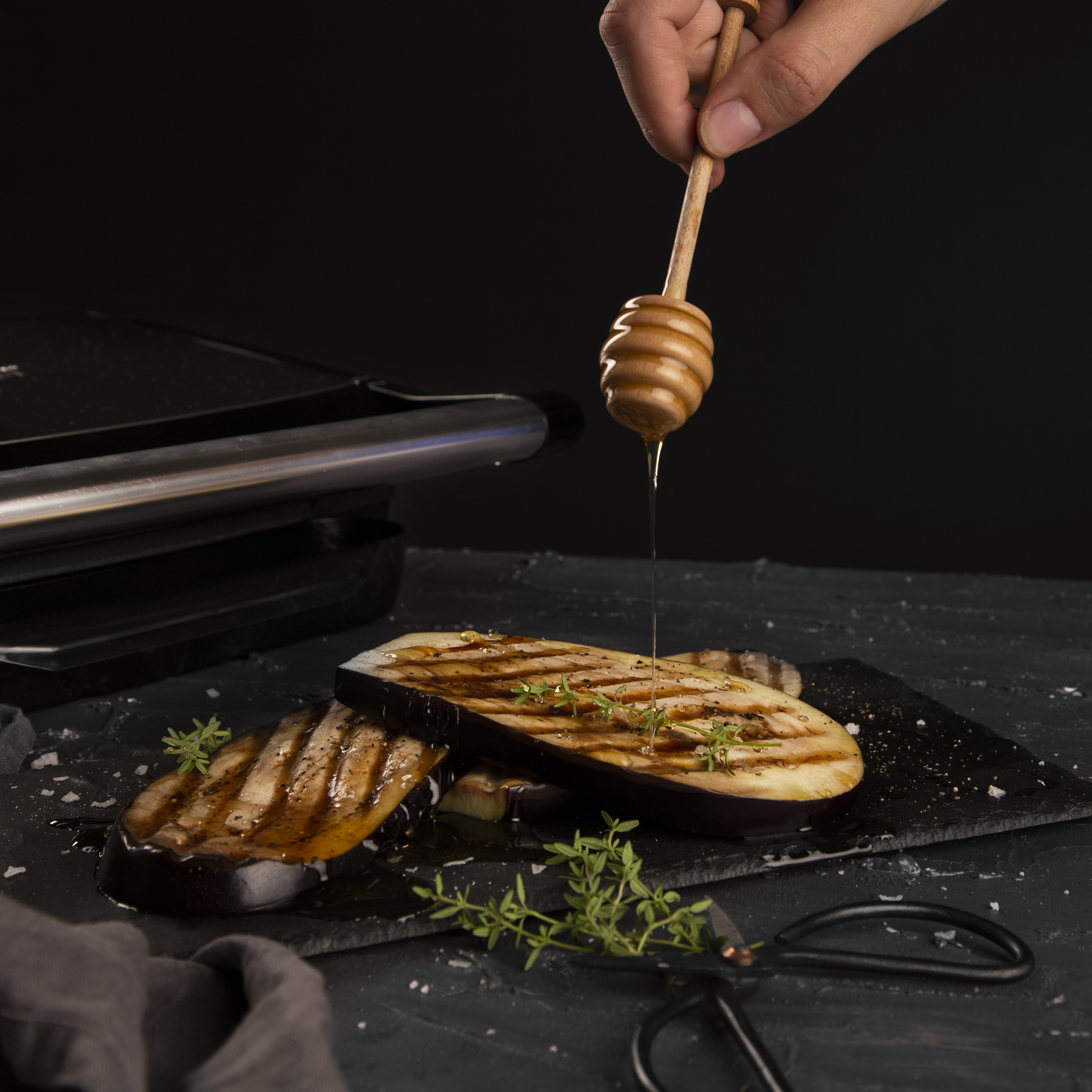Grilled eggplant slices with honey drizzled over them on a dark surface.