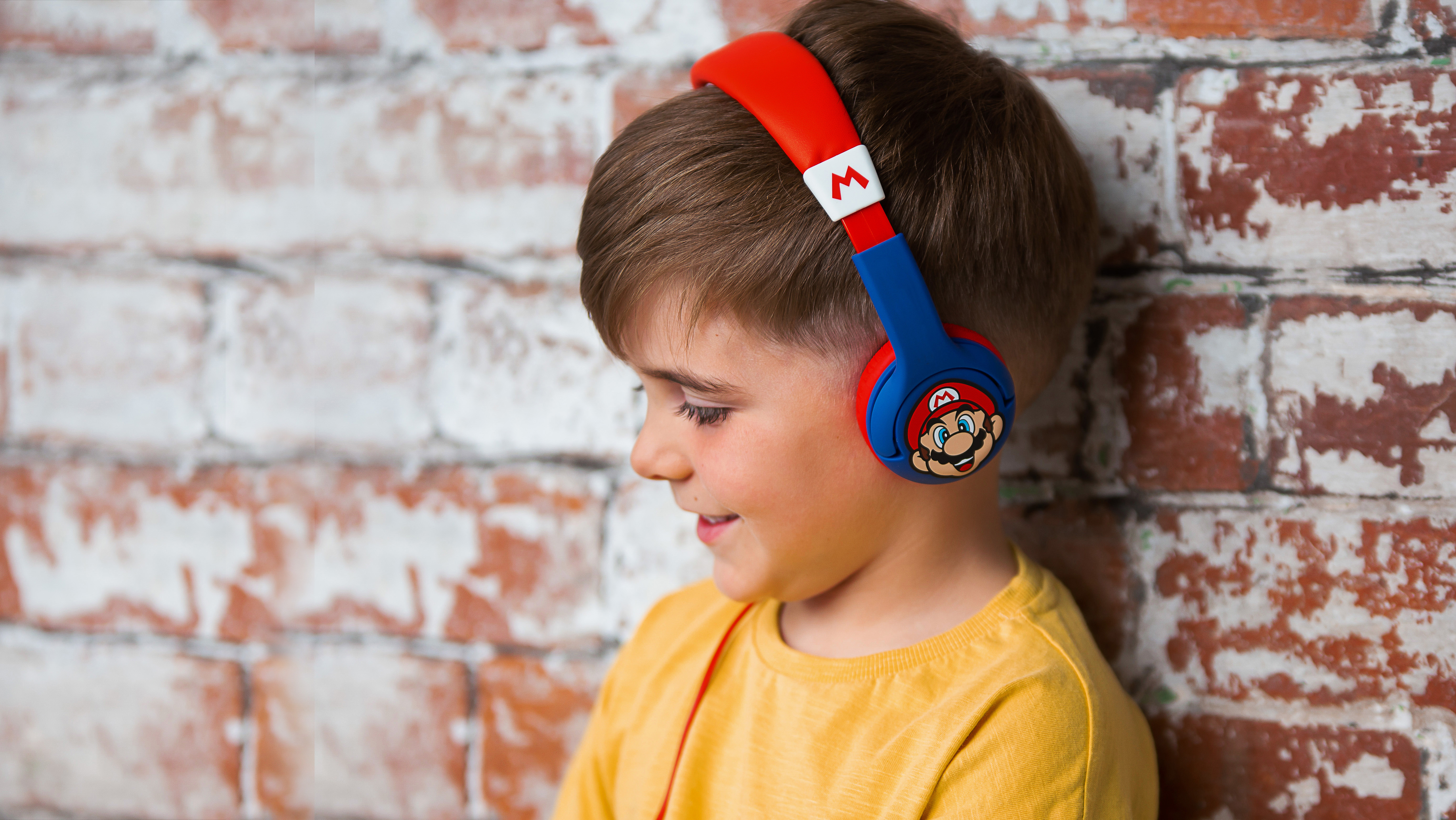 Un ragazzino con cuffie a tema Mario sorride. È vicino a un muro di mattoni.
